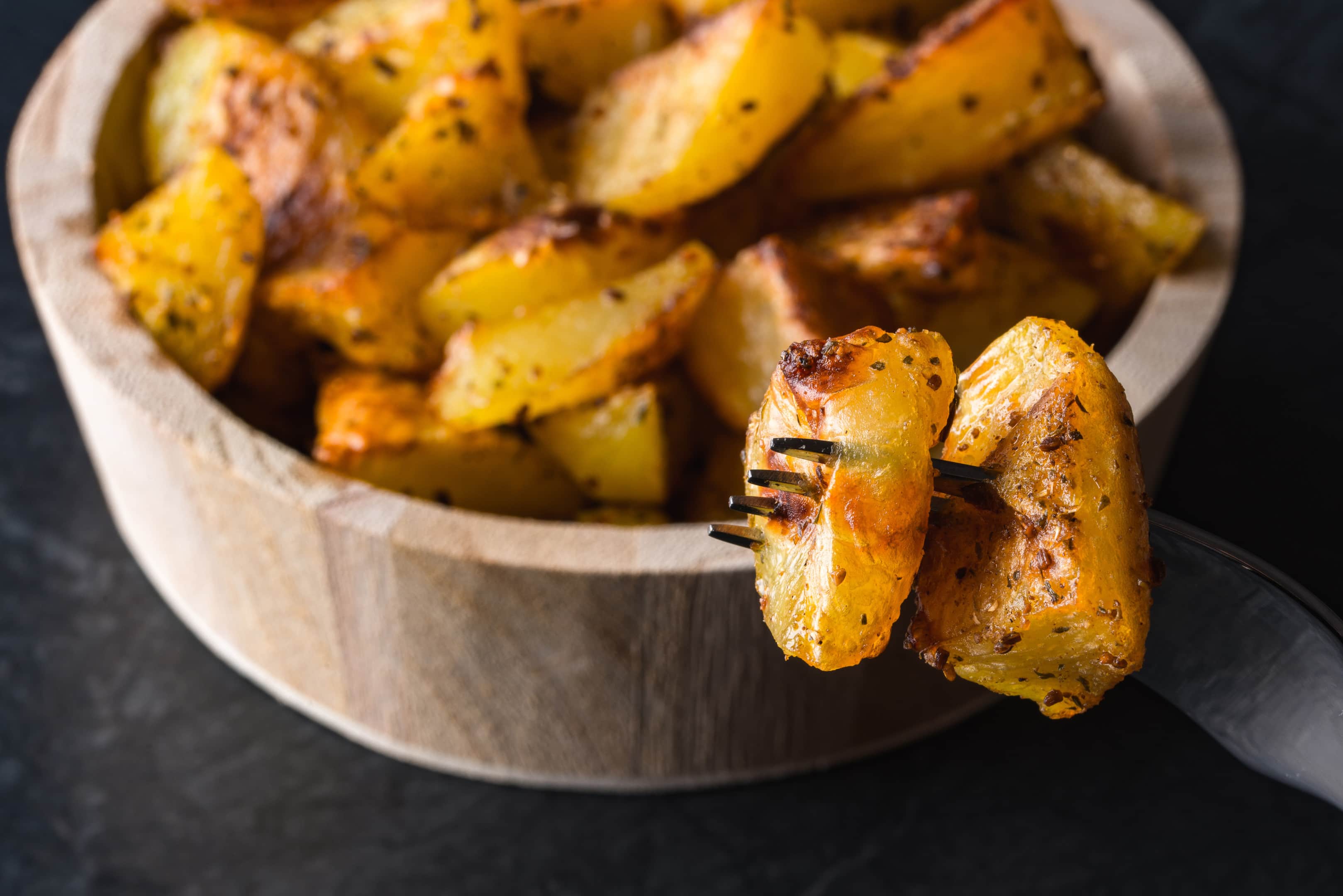 Backed potatoes in wooden bowl on black surface