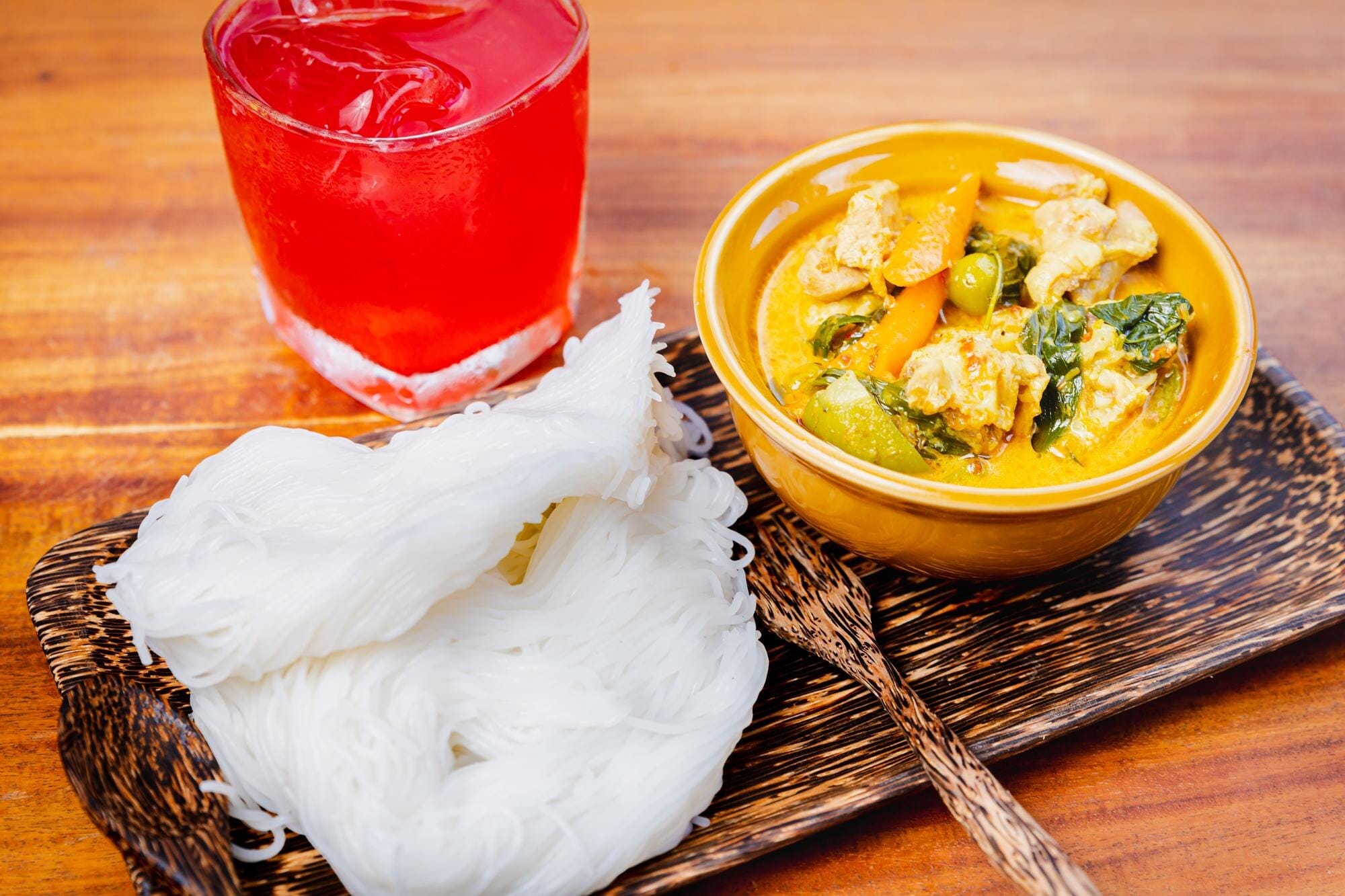 Bowl of yellow curry with rice noodles on a wooden board