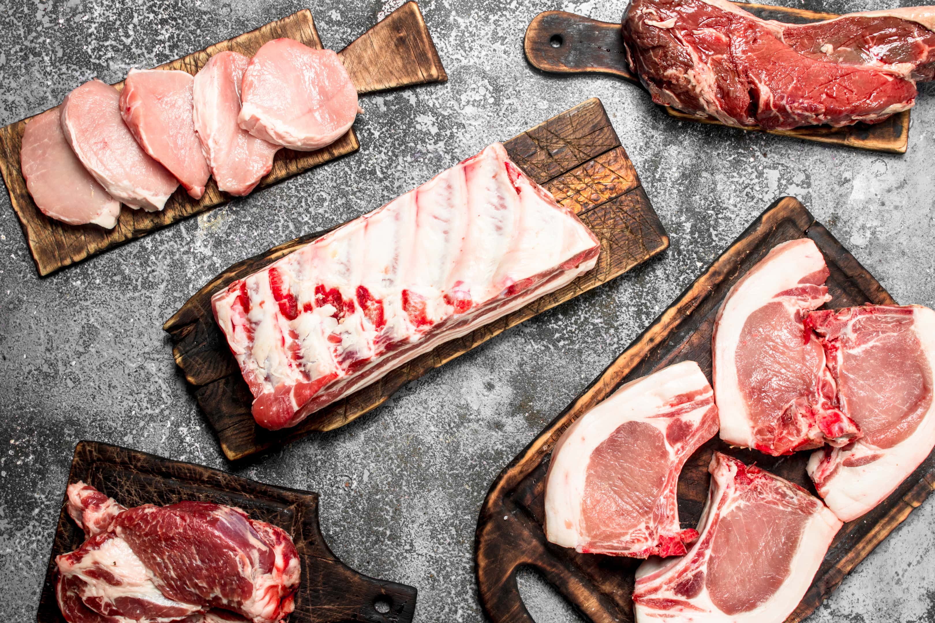 Different types raw meat on boards on rustic background