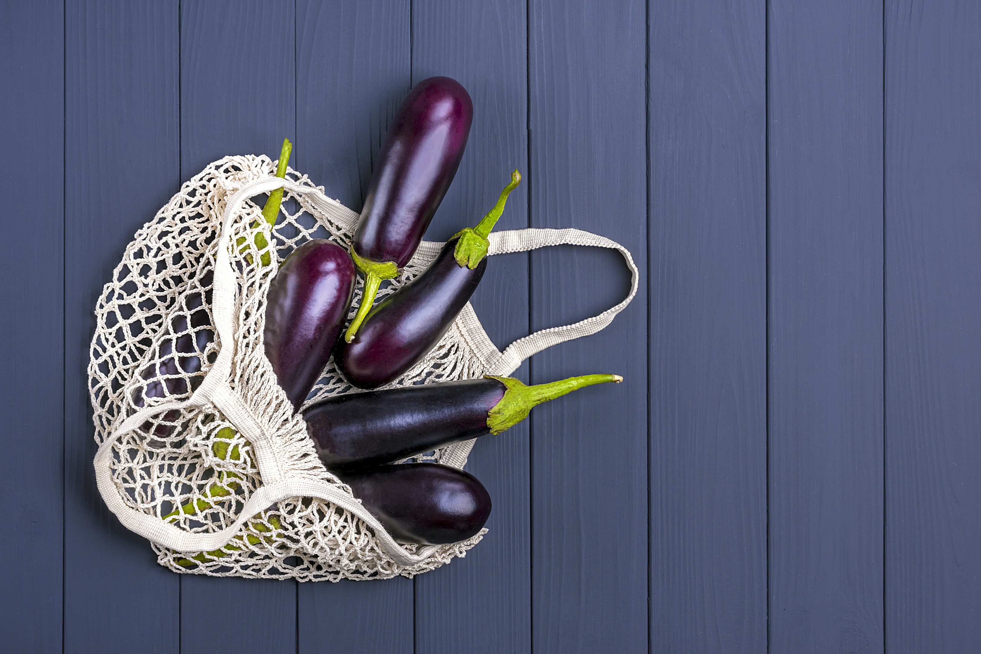 Eggplants in eco friendly mesh shopping bag on grey wooden table