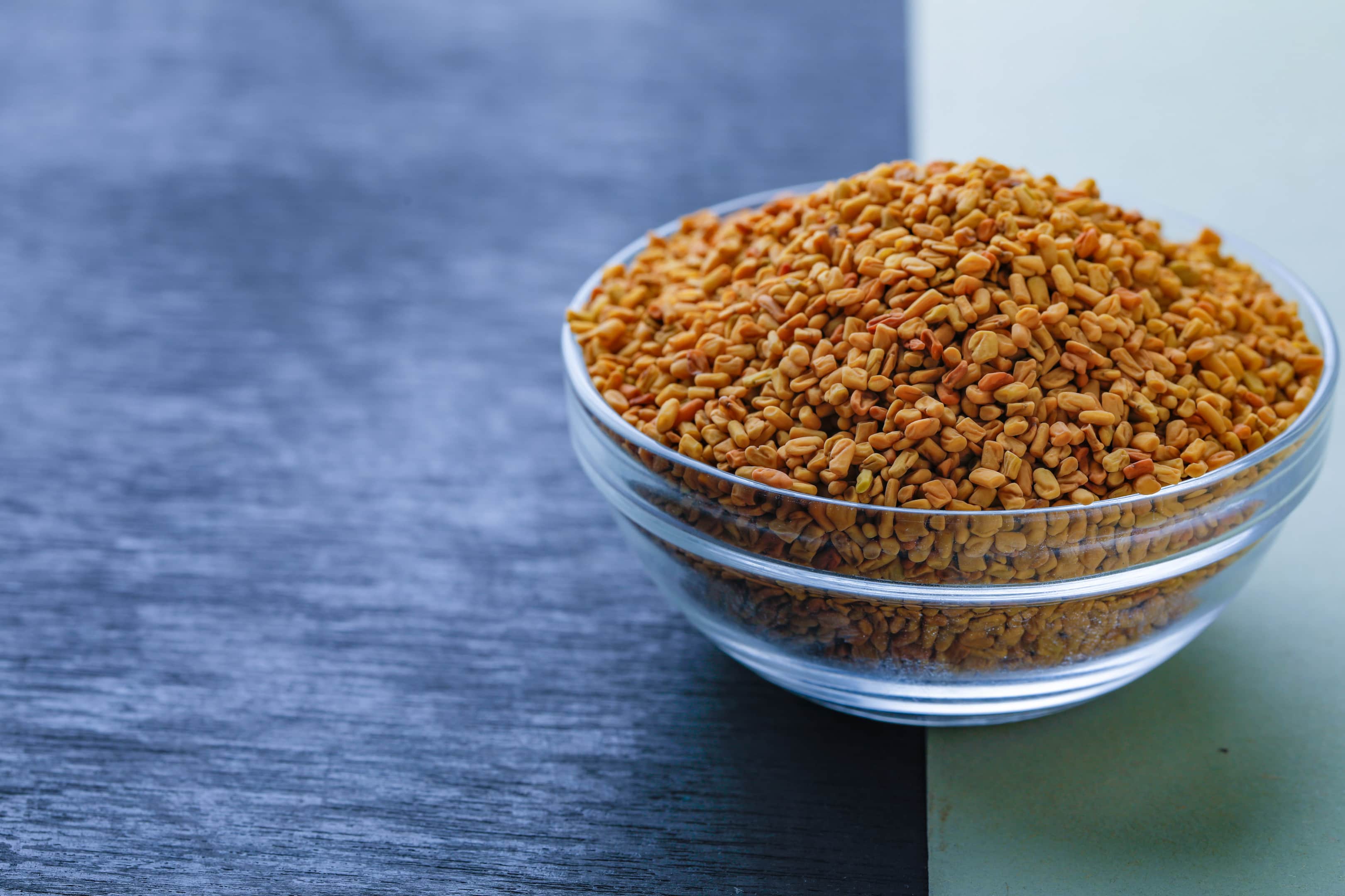 Fenugreek seeds glass bowl on two colored wooden table