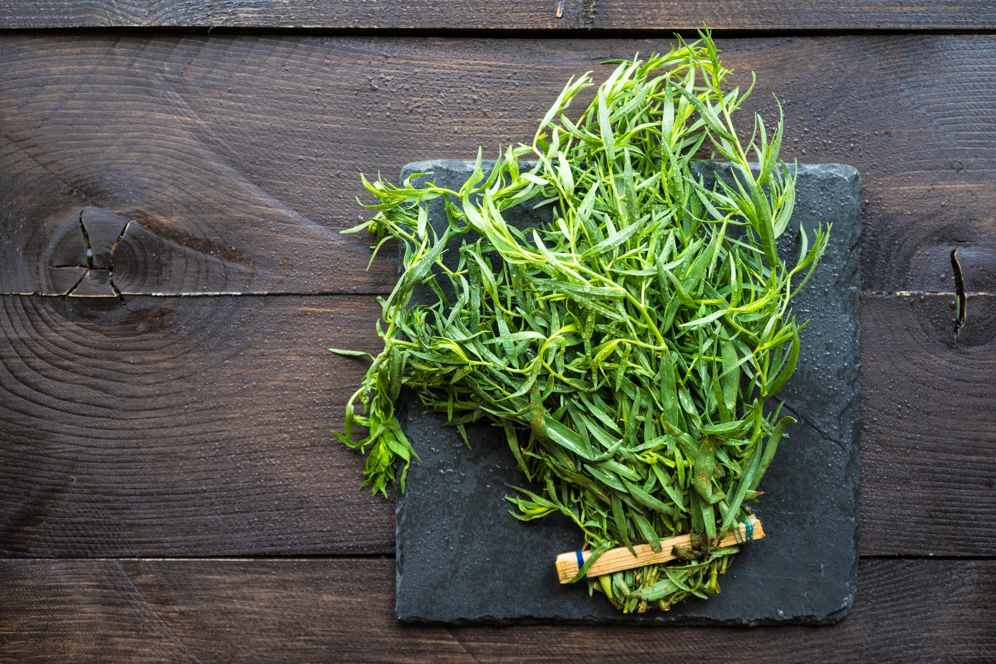 Fresh green tarragon on stone board on wooden table
