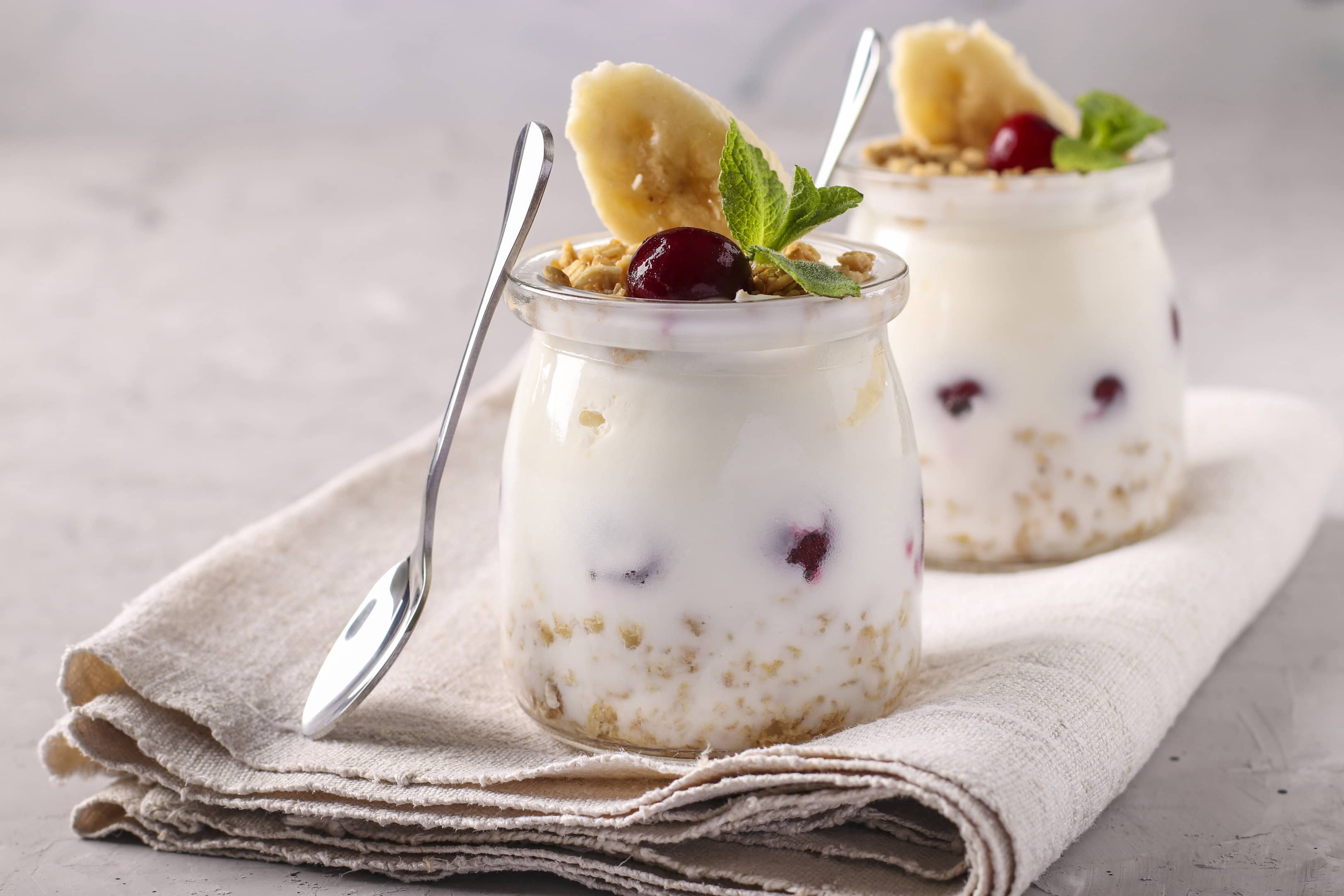 Granola crispy honey muesli with berries, banana and natural yogurt, a delicious and healthy breakfast, located in glass jars on a gray background, Closeup