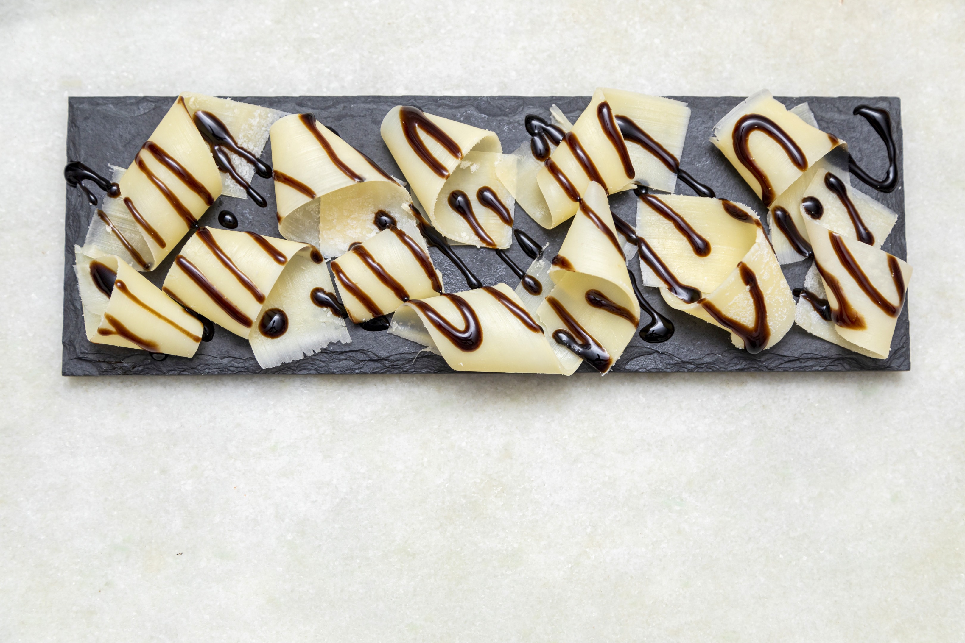 Parmesan cheese flakes with balsamic vinegar on black stone