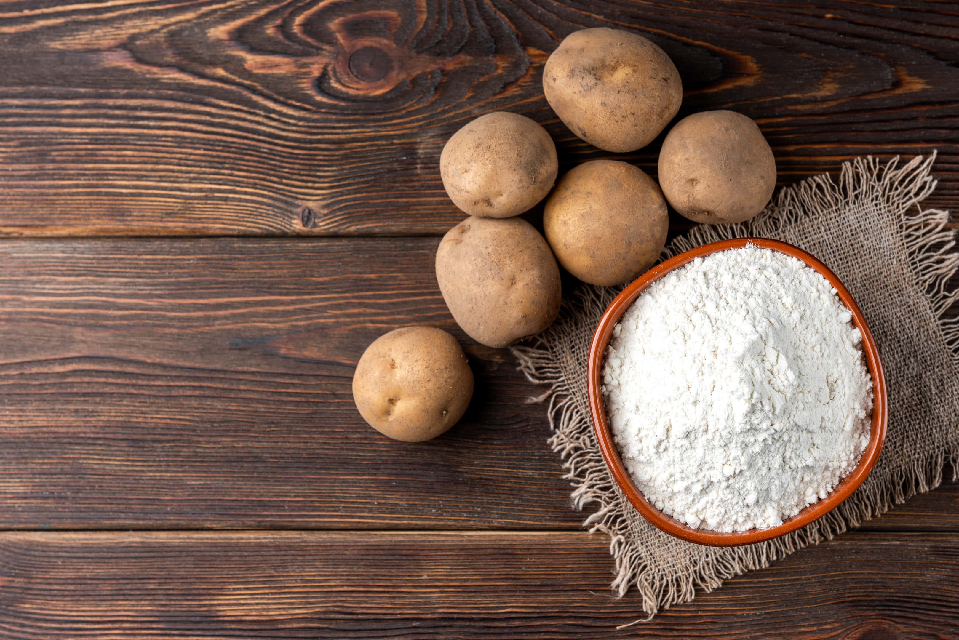 Potato starch in wooden bowl and fresh potato