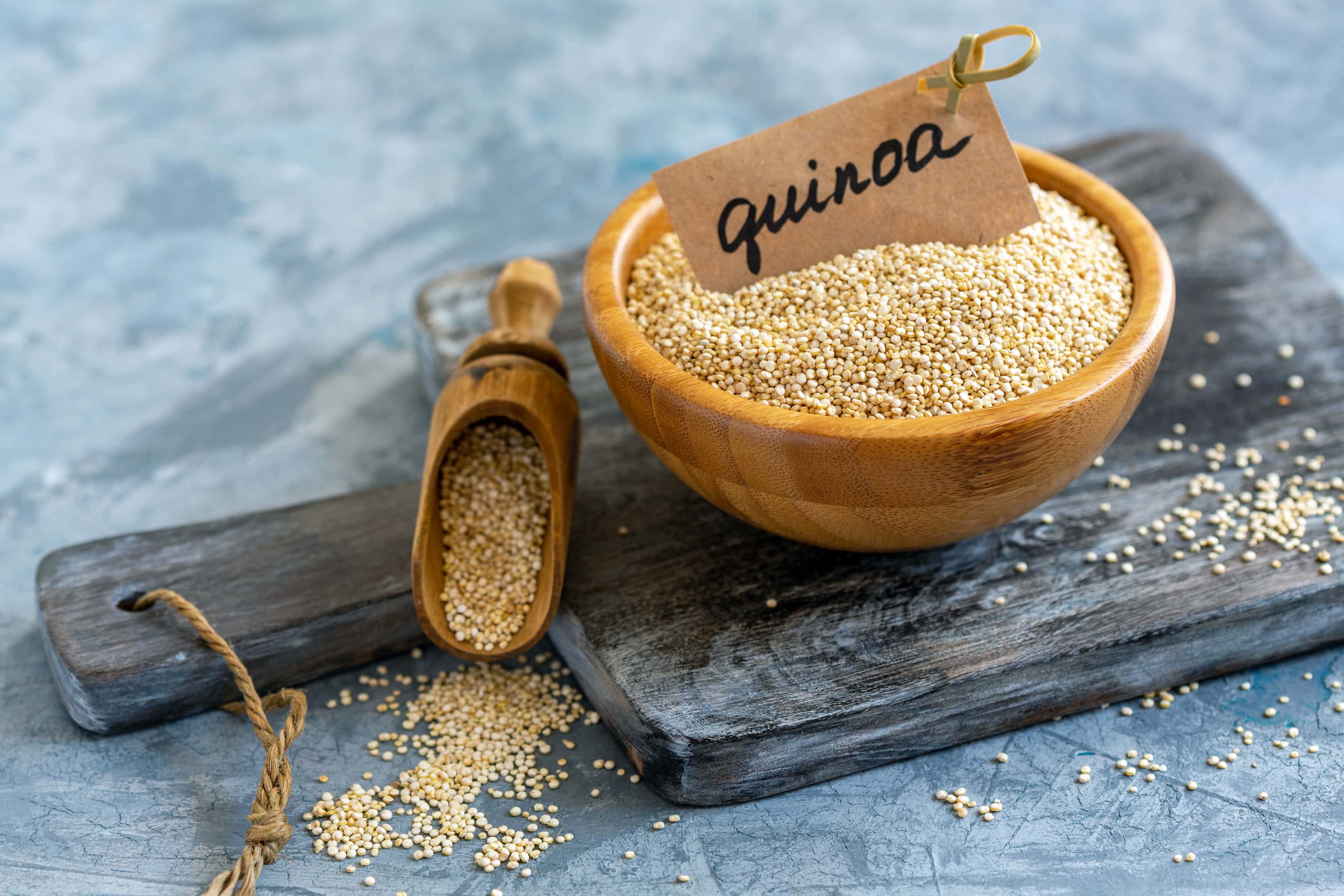 Raw white quinoa in wooden bowl on wooden board
