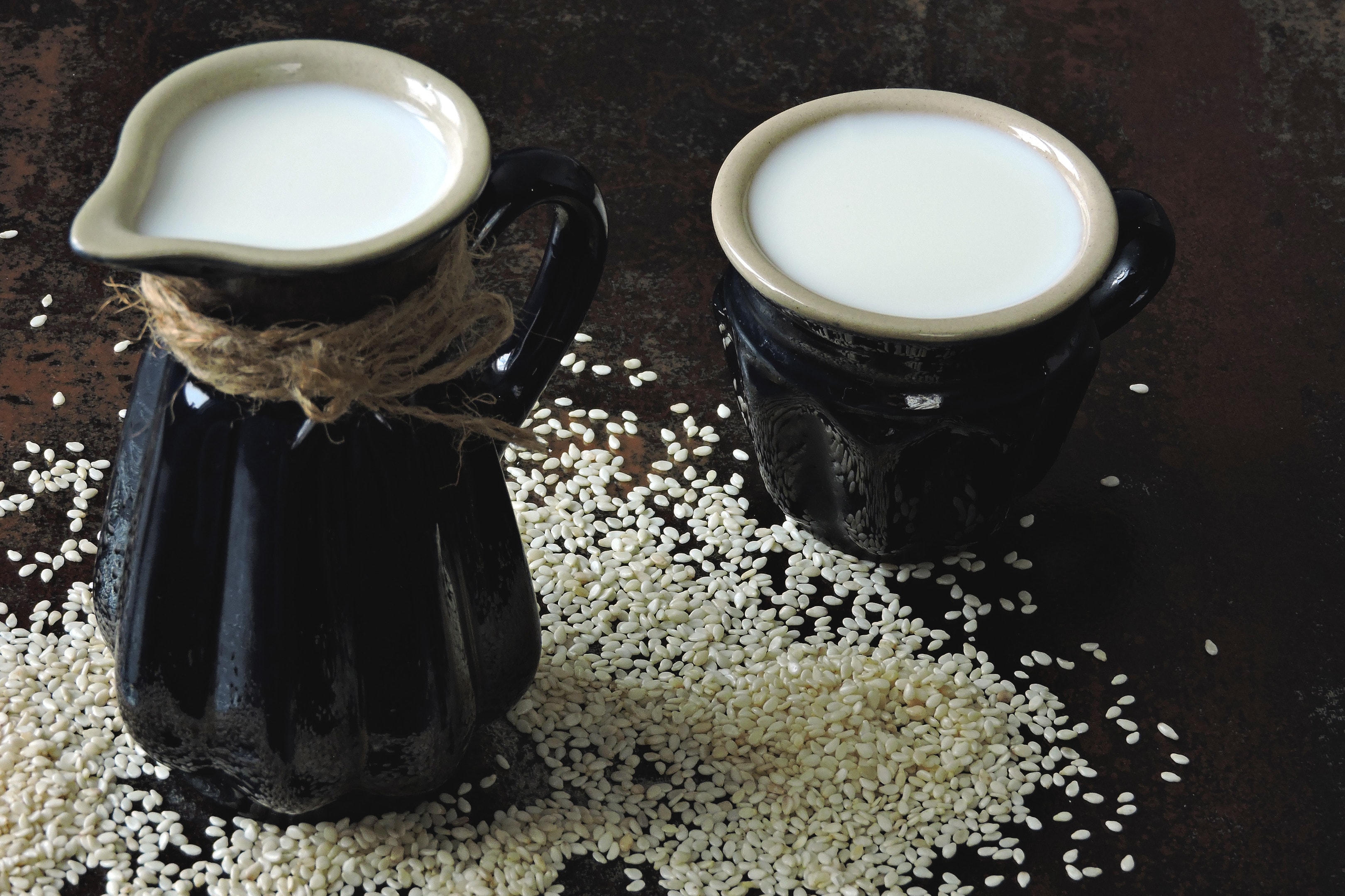 Sesame milk in jug and mug with scattered sesame seeds