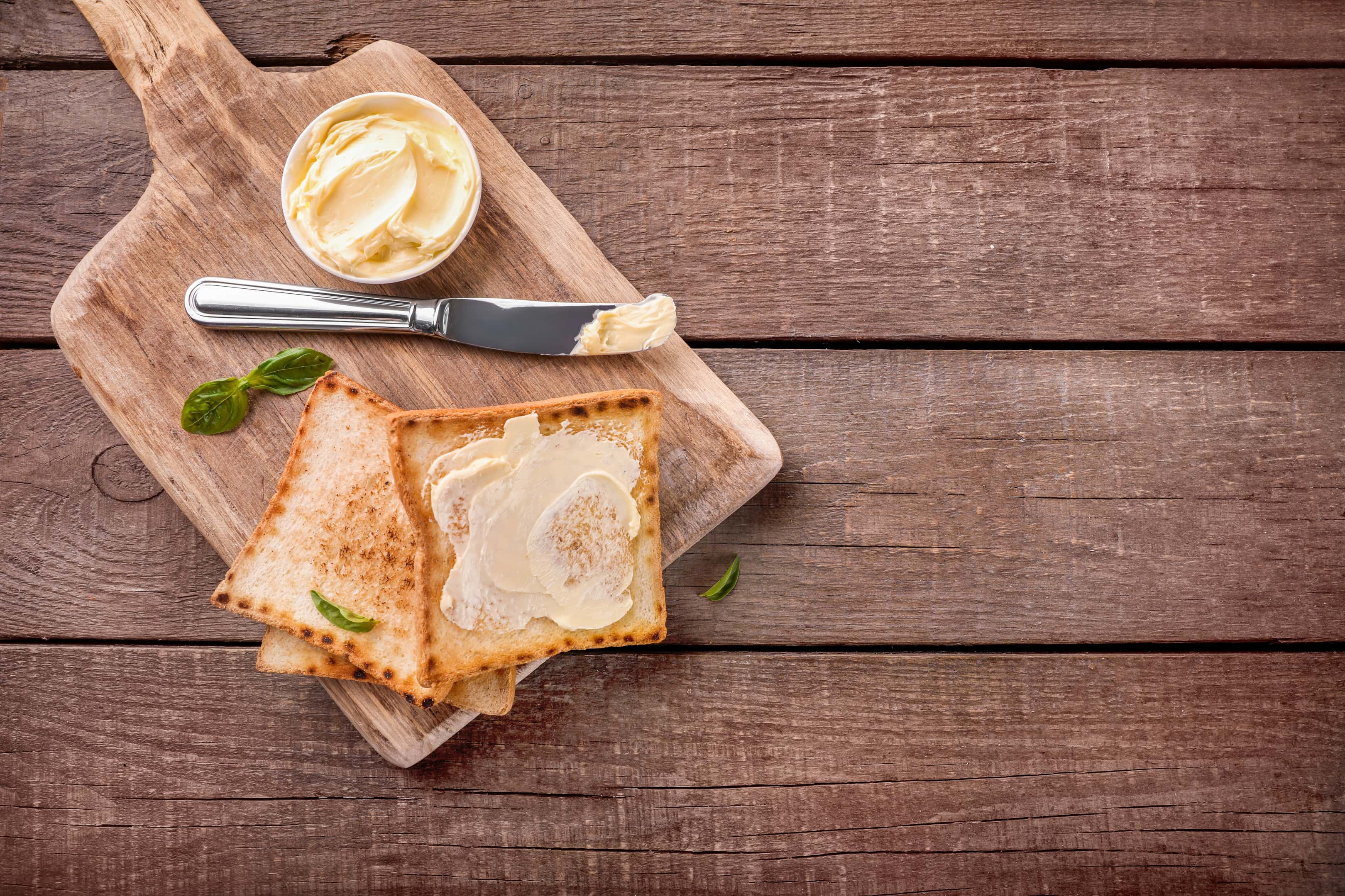 Slices of toast bread with margarine on a wooden cutting board
