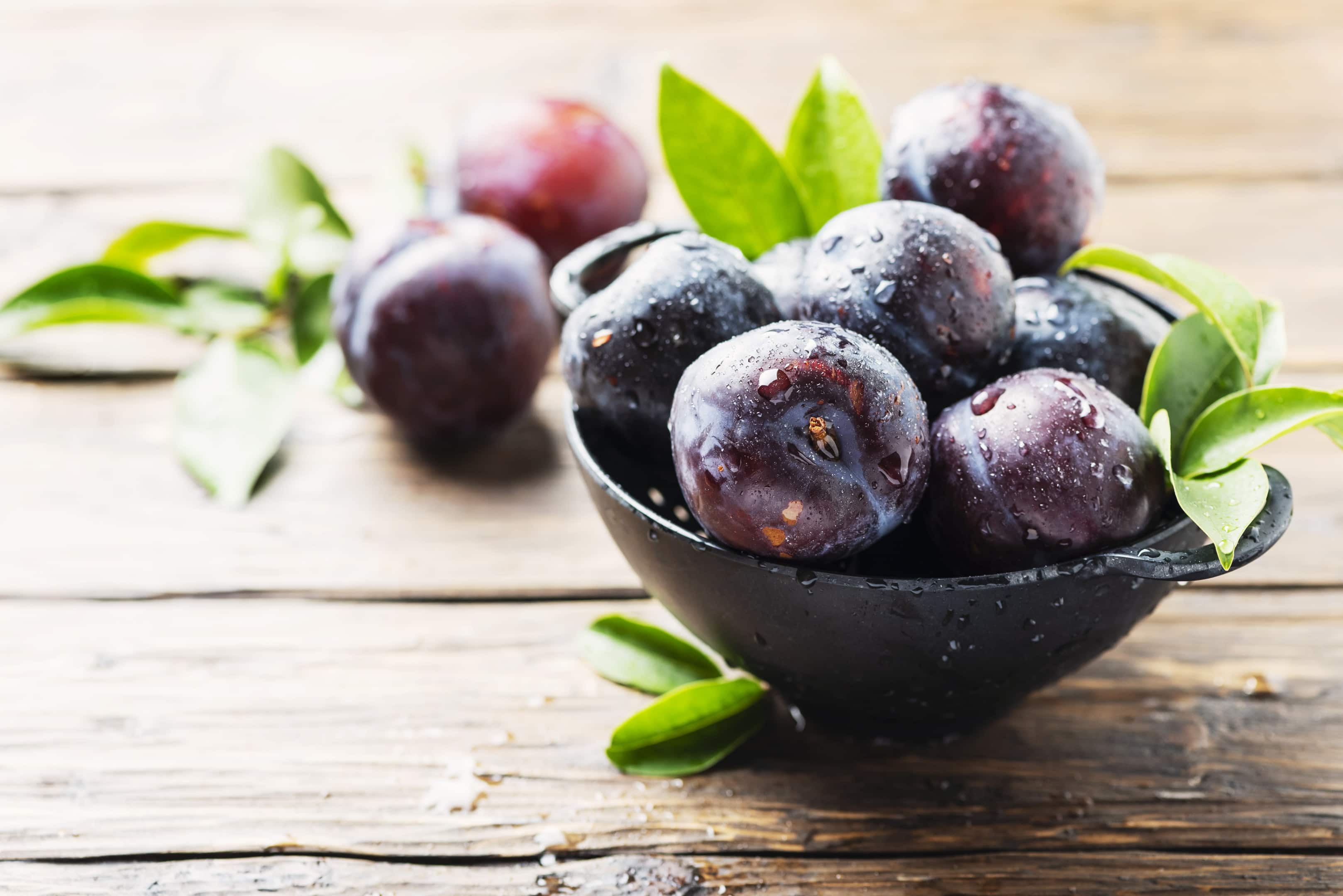 Sweet red plums in bowl on wooden table