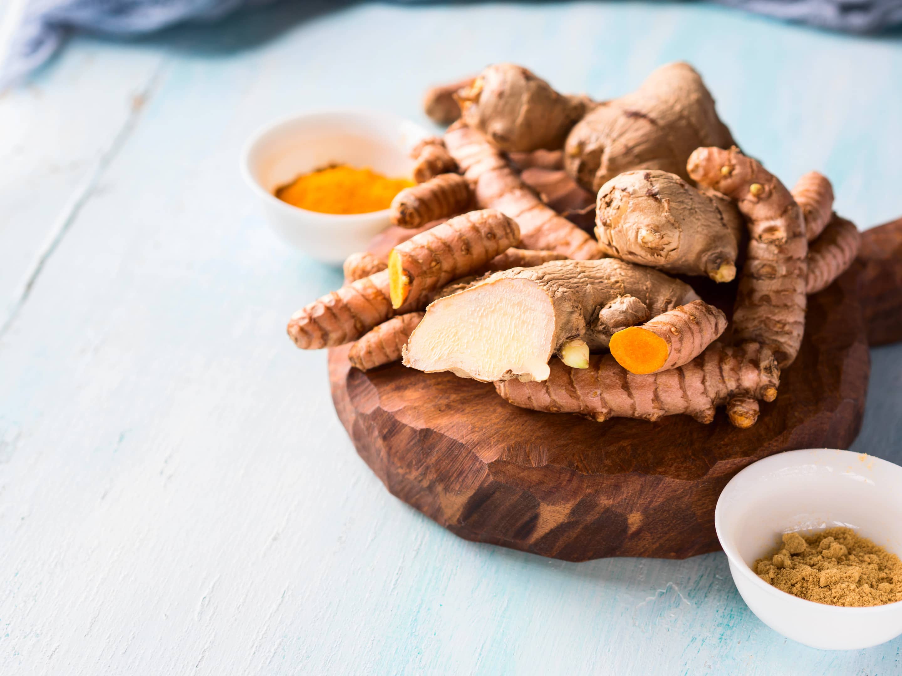 Turmeric and ginger powder and roots on wooden board