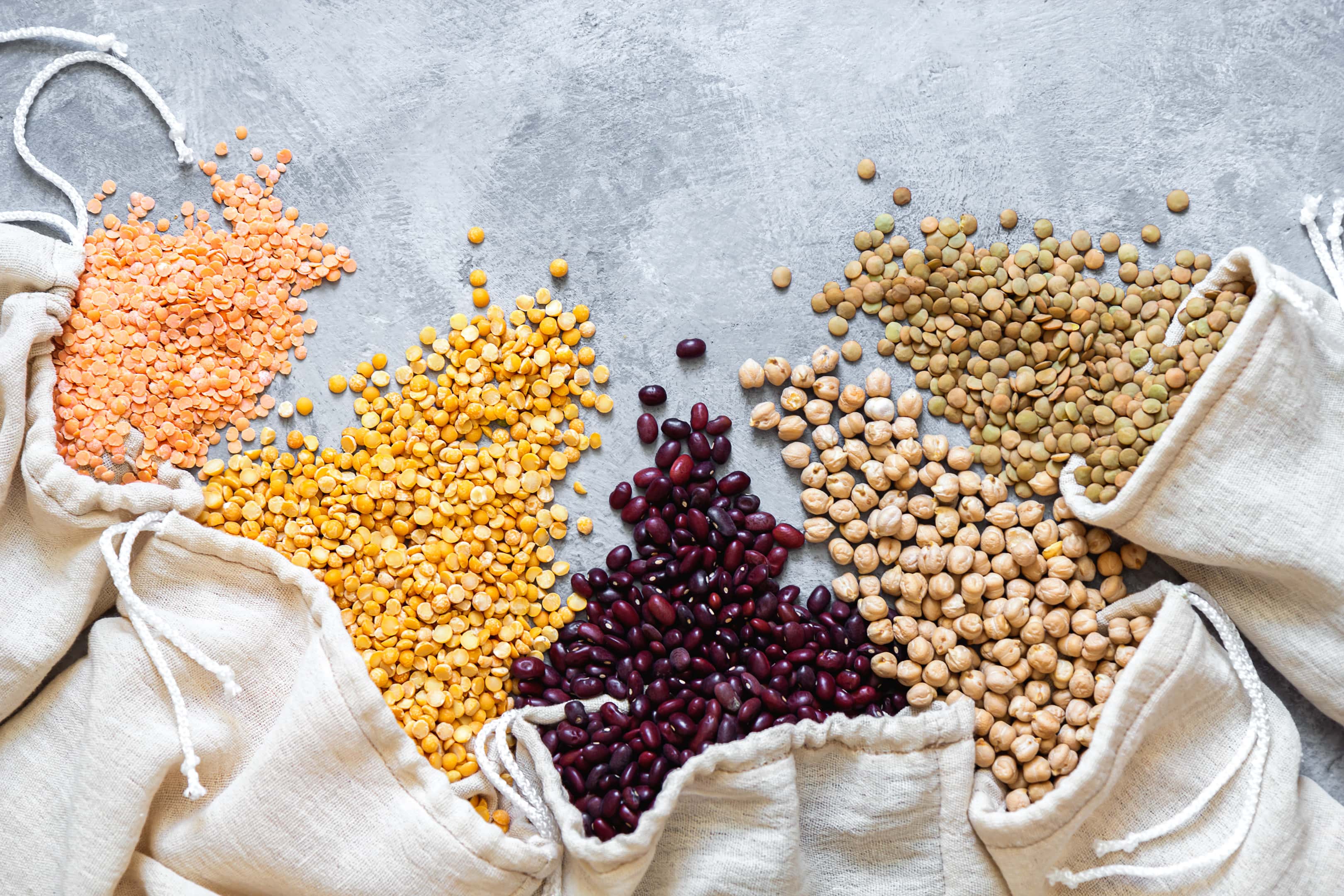 Various legumes spill from eco bags