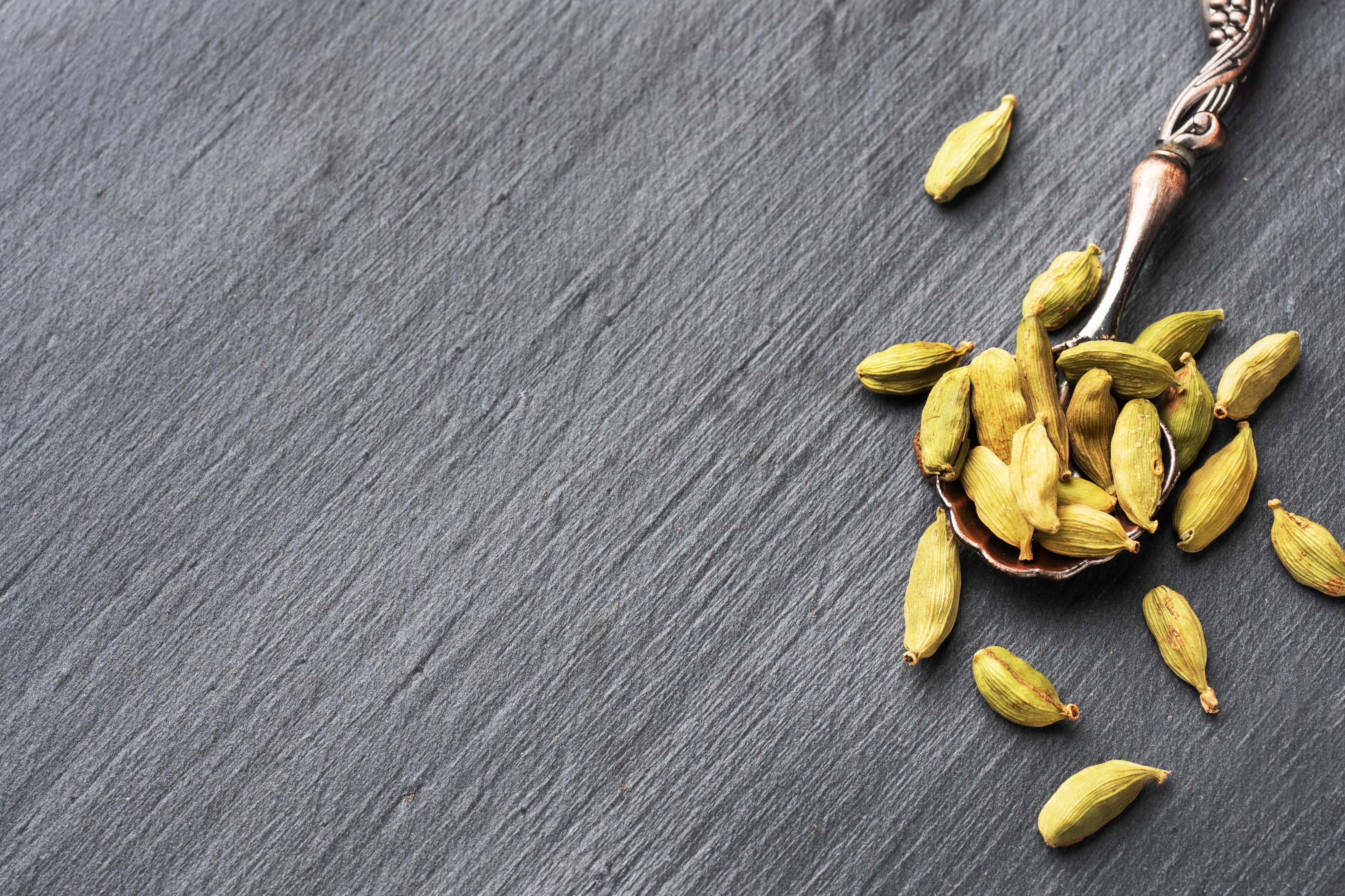 Whole cardamom in metal spoon on wooden table