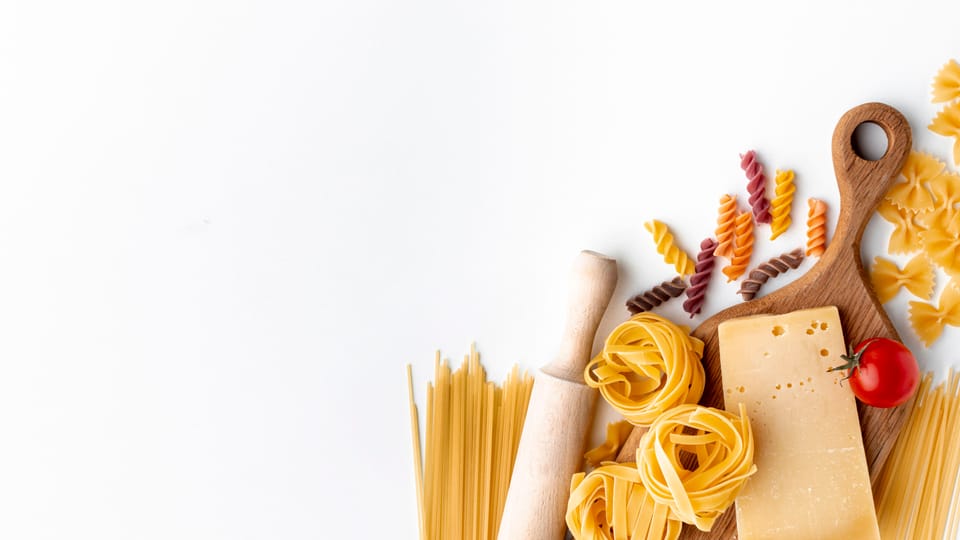 Mix of uncooked pasta and hard cheese on white background