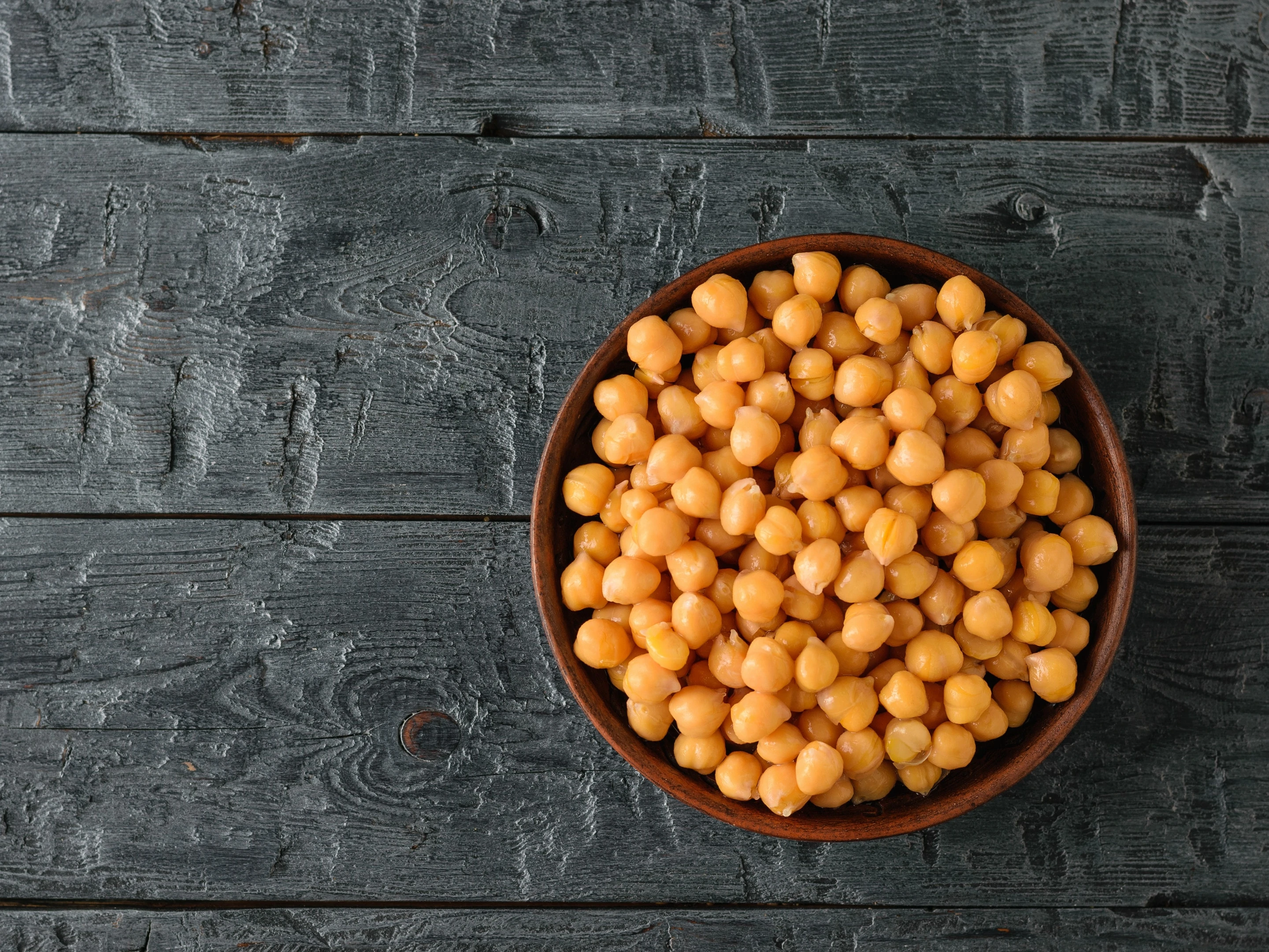 Boiled chickpeas in clay bowl on black wooden table