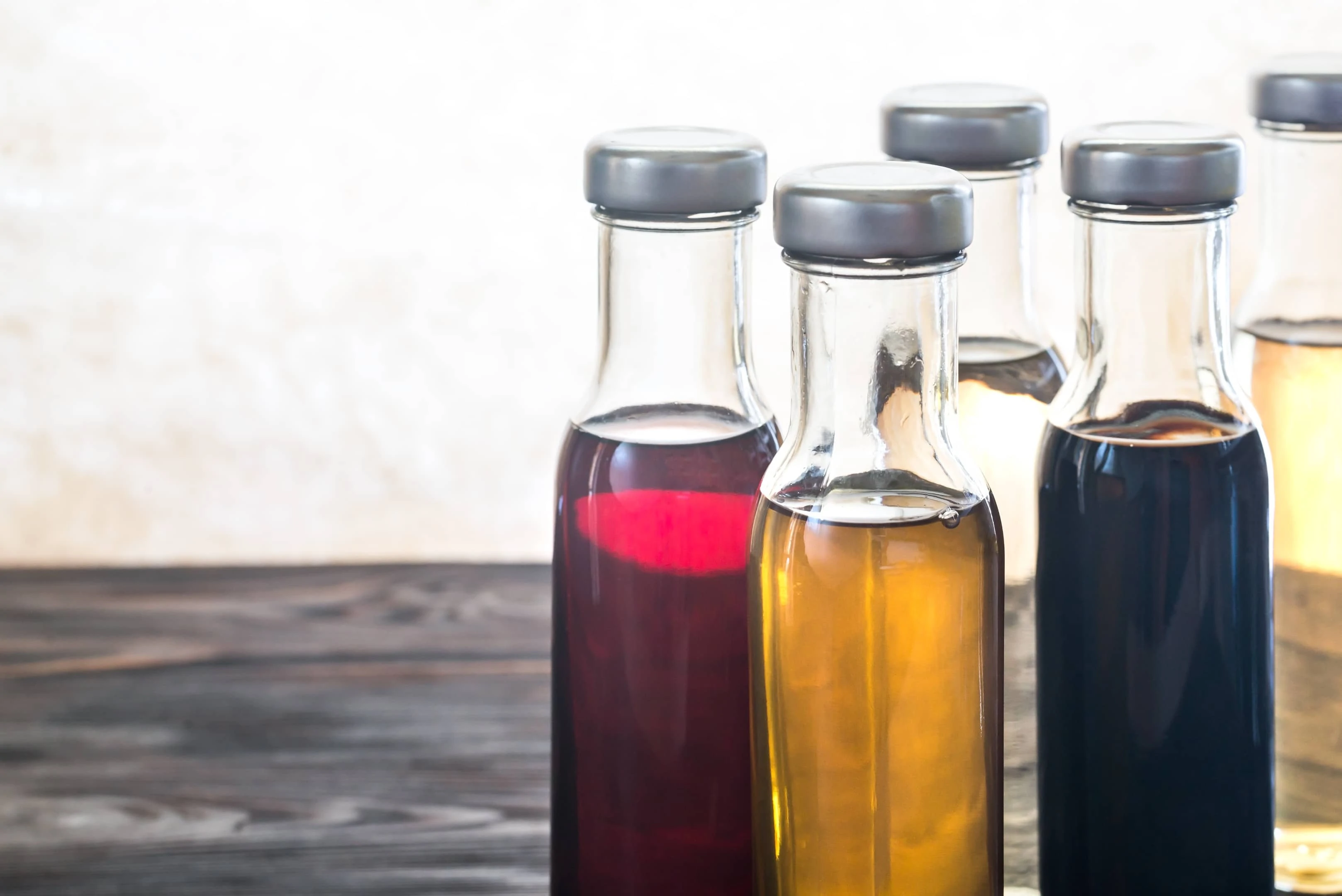 Bottles with different kinds of vinegar on wooden table