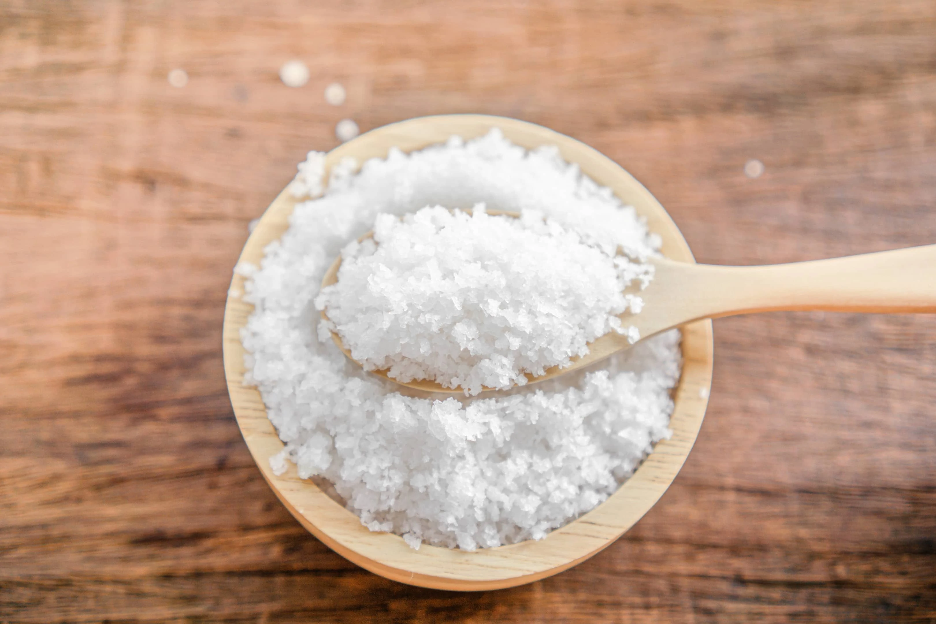 Closeup of salt in bowl with spoon on wooden table