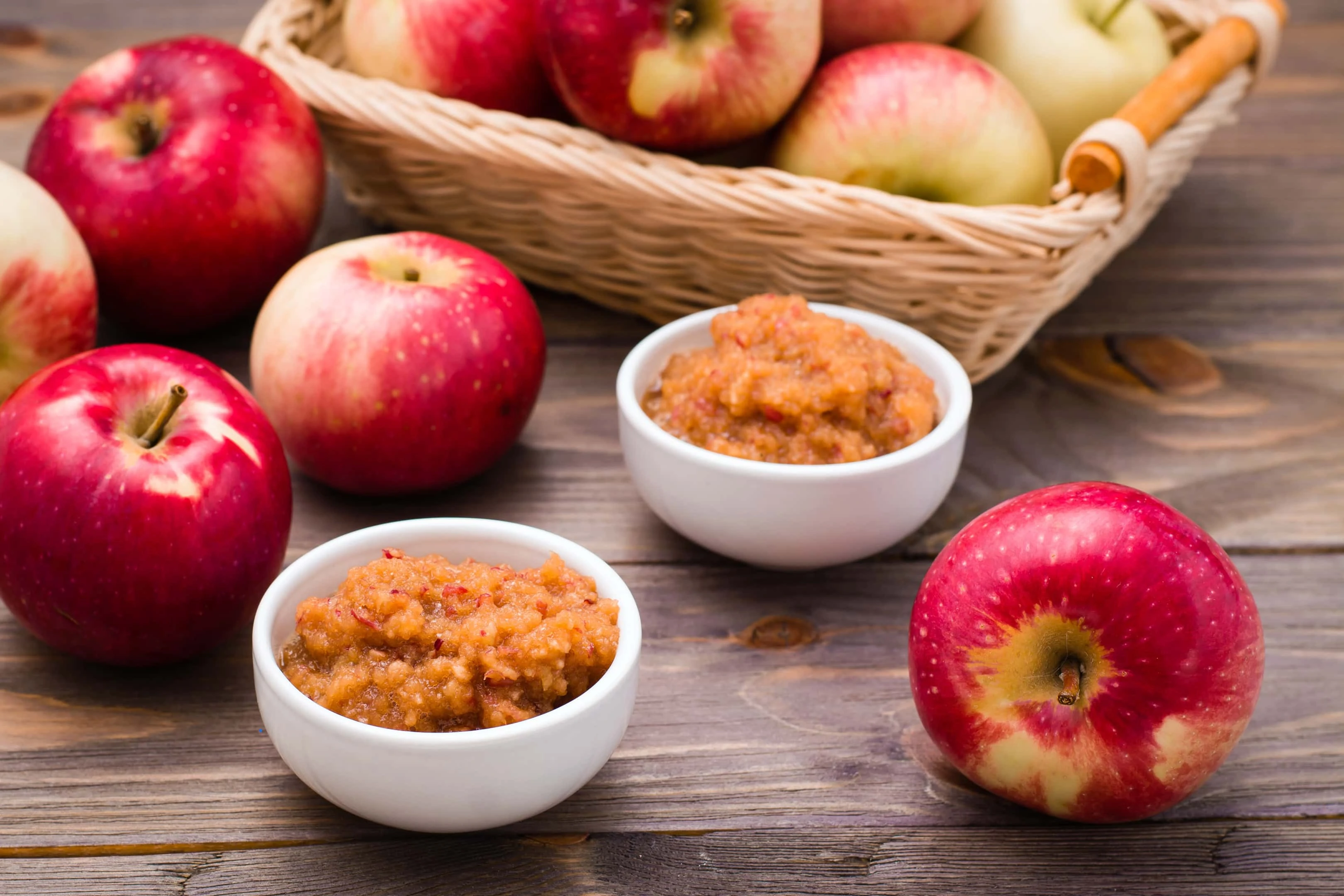 Fresh applesauce in bowls with fresh red apples on a wooden table