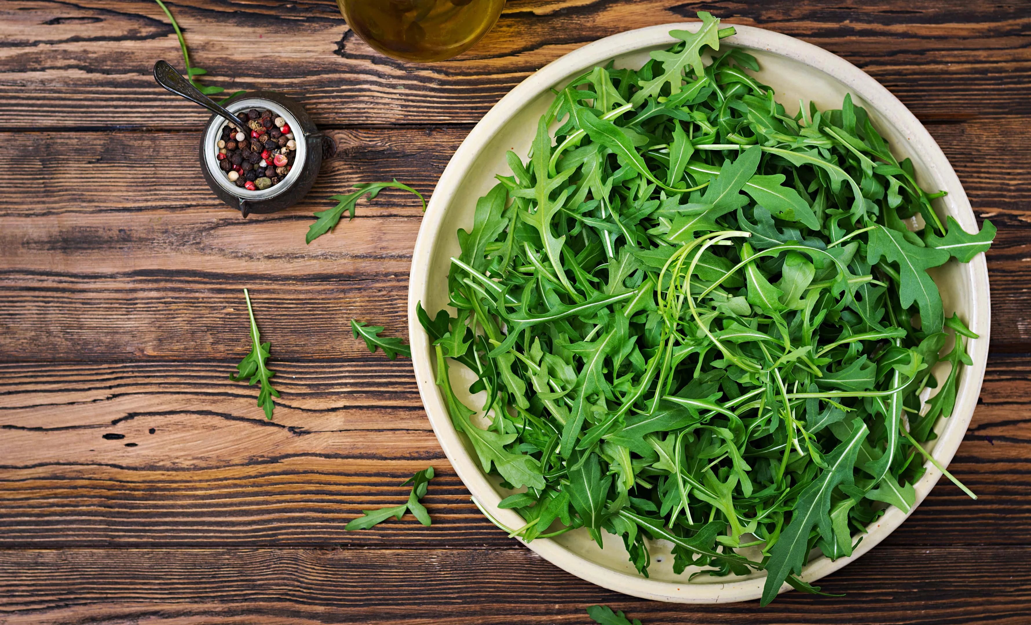 Fresh arugula leaves in a white bowl on a wooden table