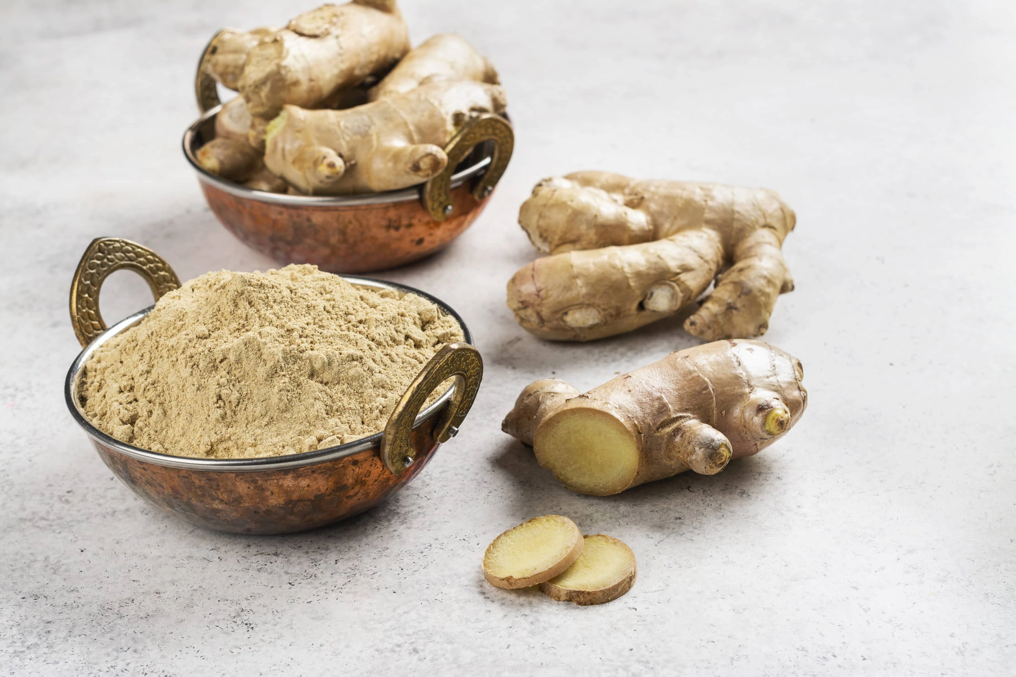 Fresh ginger root and ginger powder in copper bowl