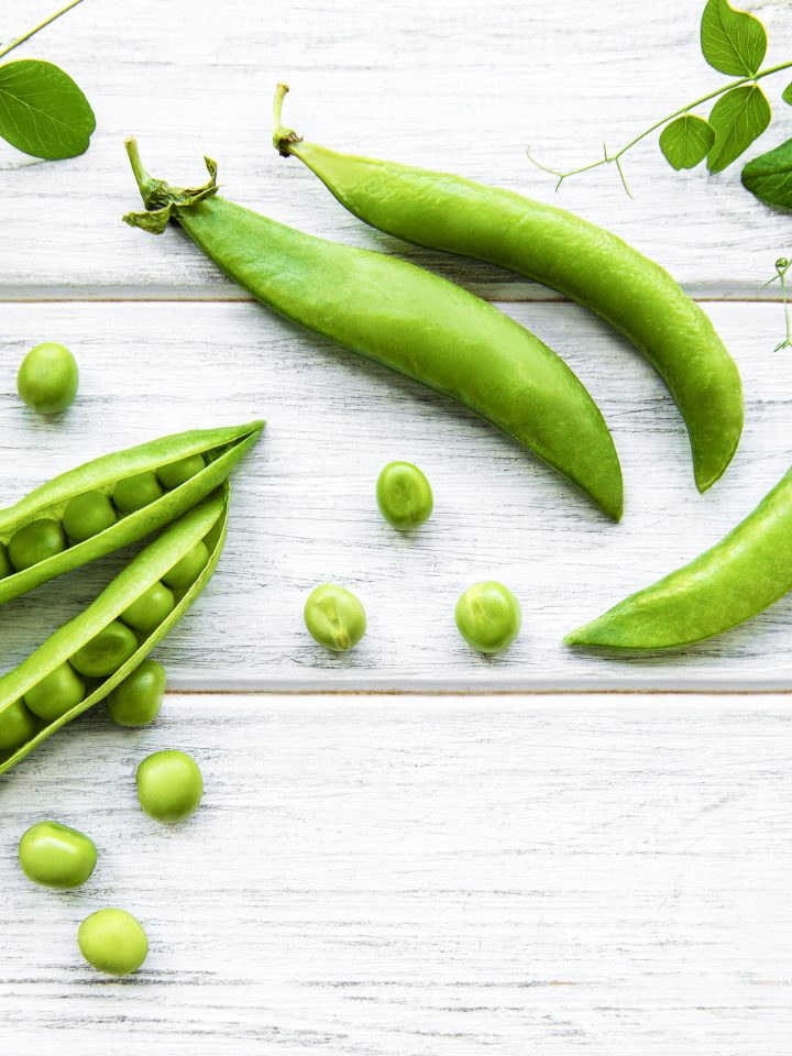 Green peas and pea pods on white wooden background