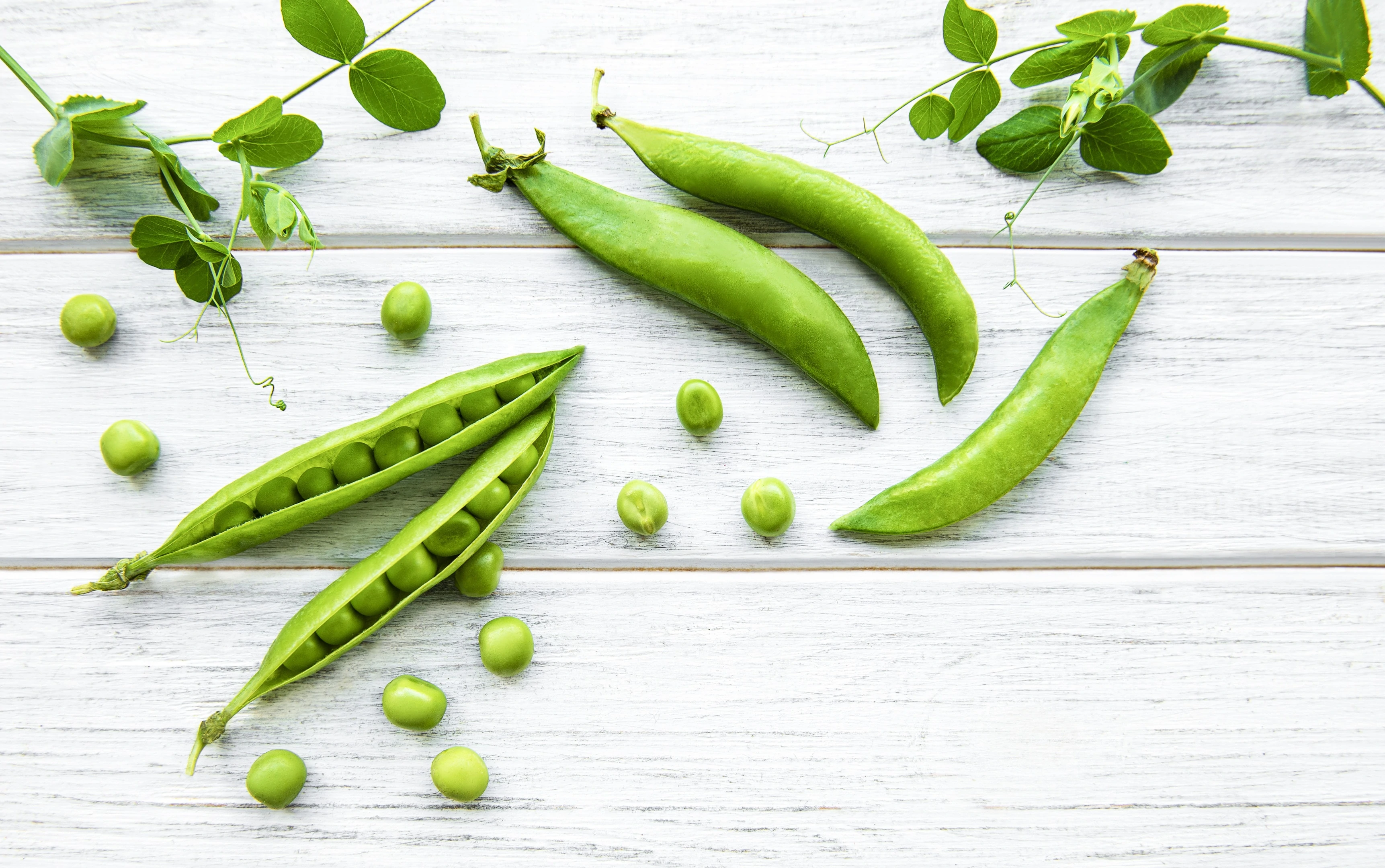 Green peas and pea pods on white wooden background