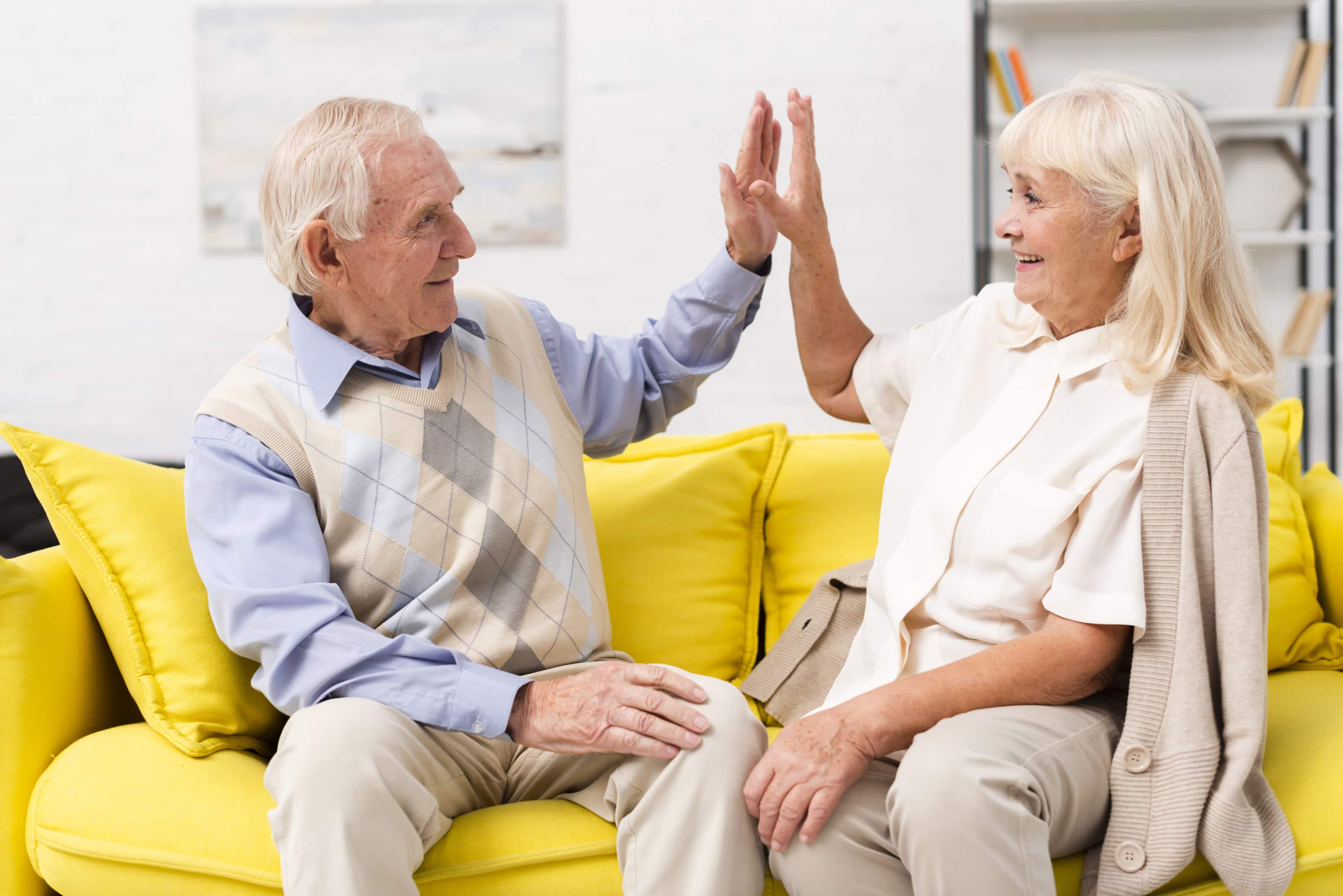 Old man and woman high fiving on yellow sofa