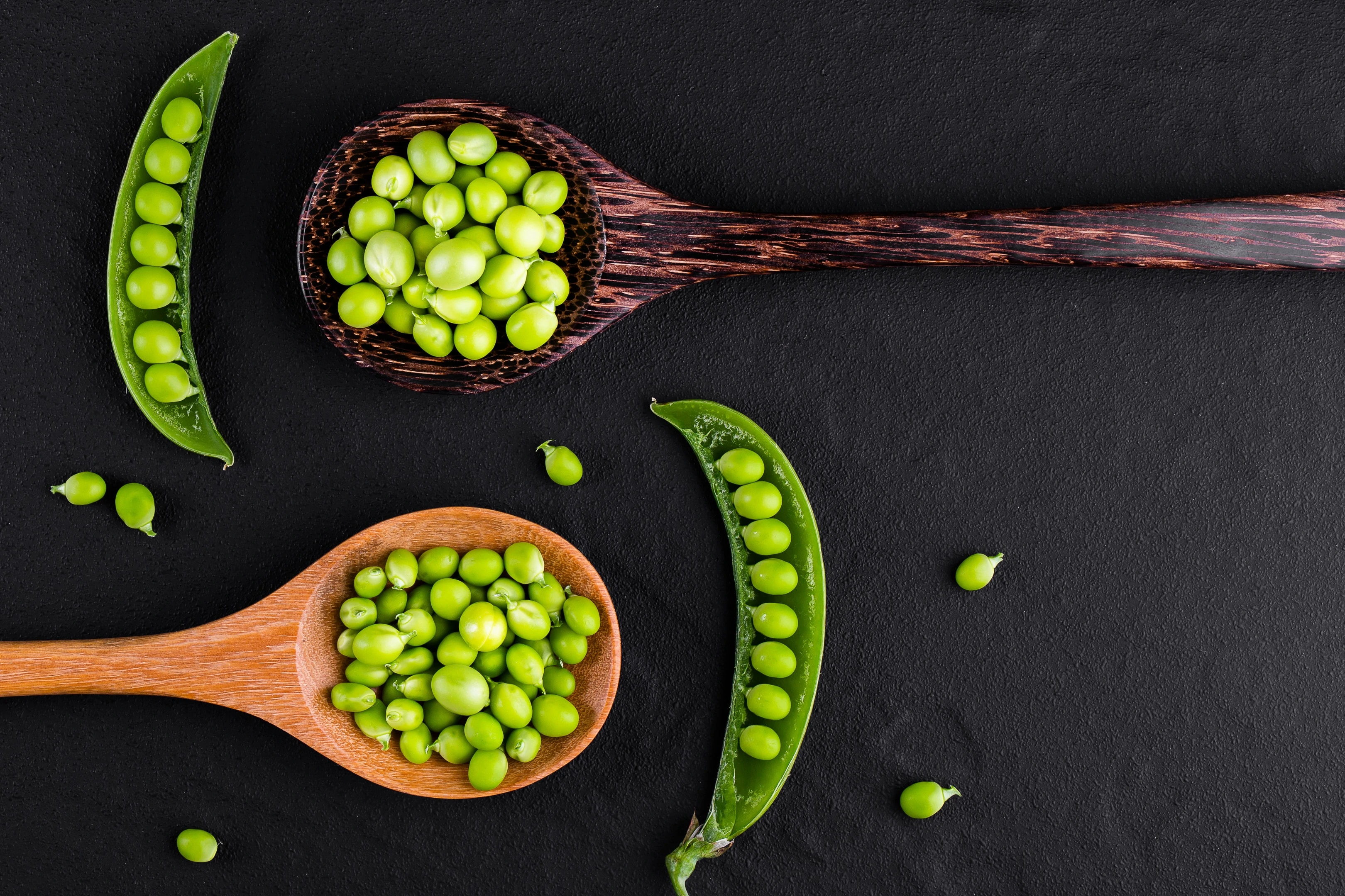 Pea pods on wooden spoons on black background