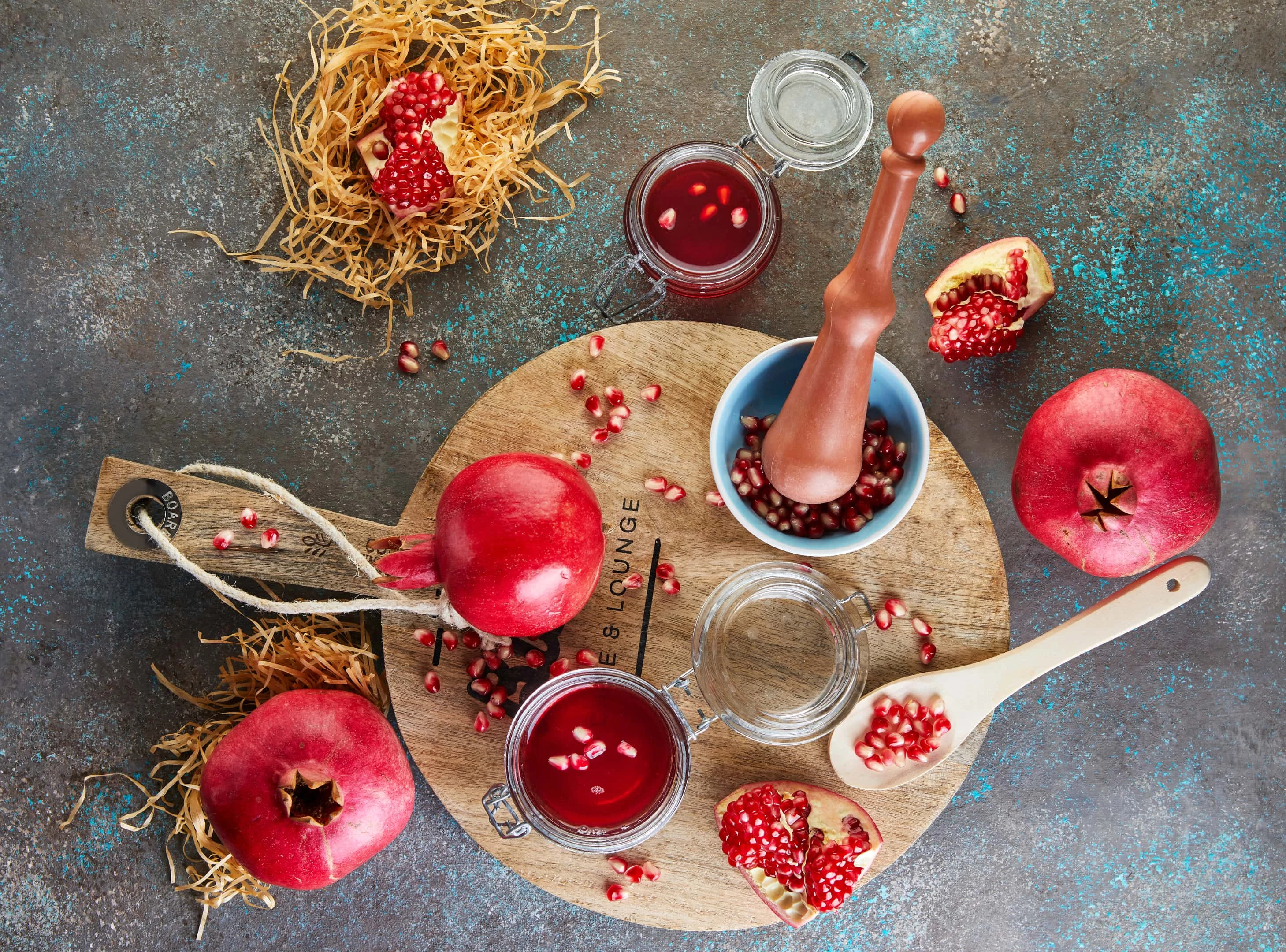 Homemade pomegranate molasses syrup in jars with pomegranate seeds on a wooden board