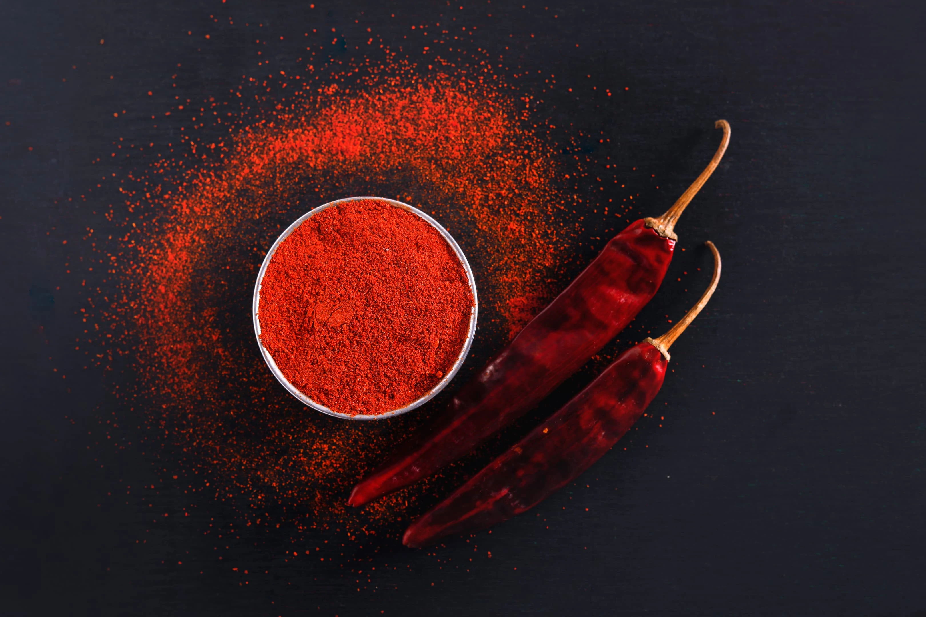 Red chili pepper flakes powder and dried red chili on black background