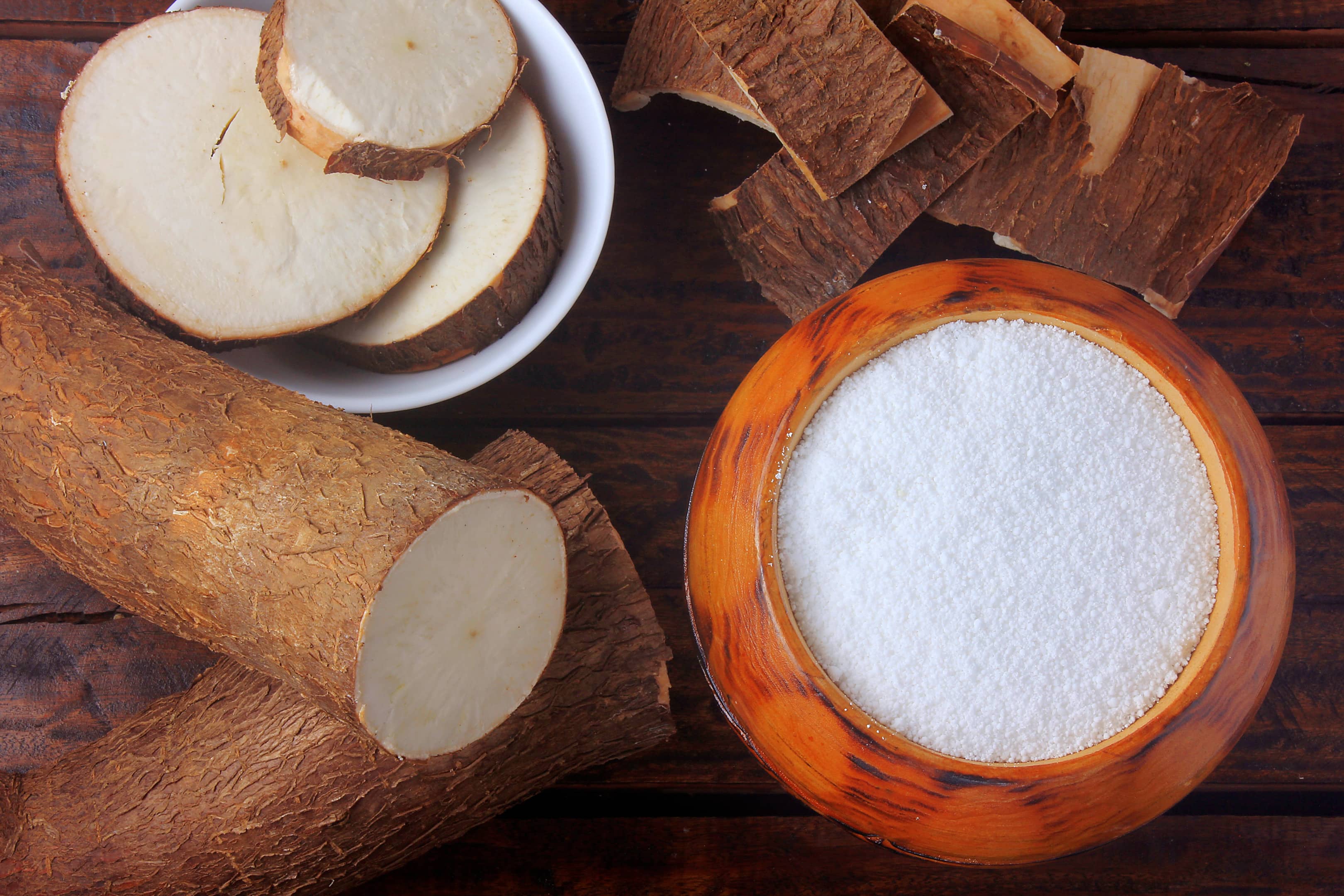 Tapioca flour in wooden bowl next to cut cassava root