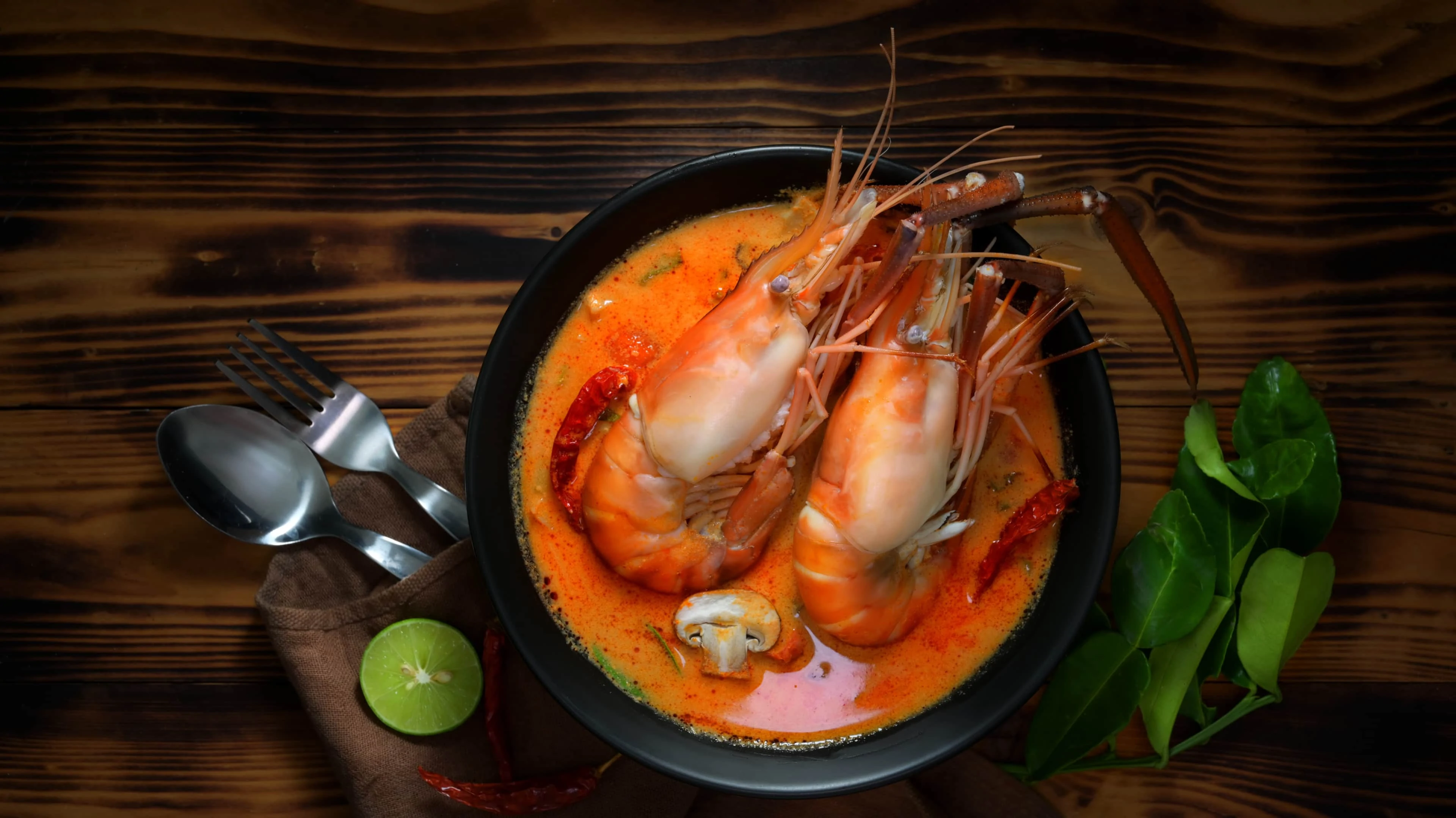Top view of Tom yum goong with prawns, spicy soup in black bowl on wooden table