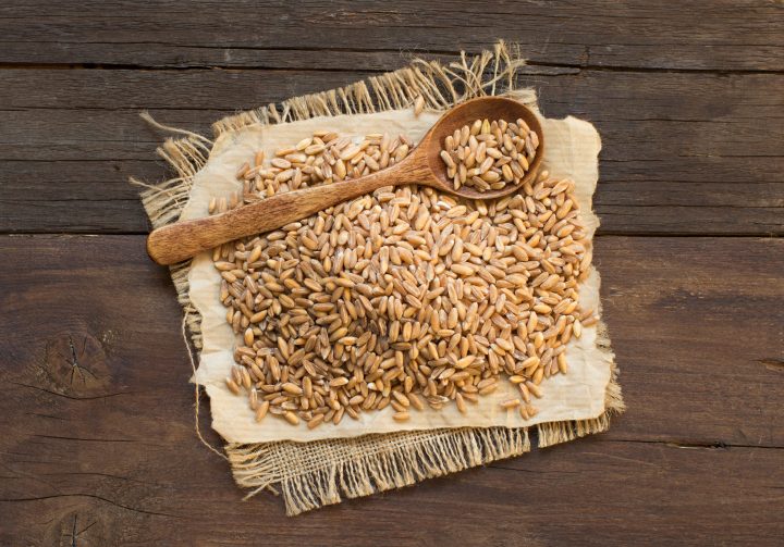 Whole unpolished spelt with wooden spoon on table