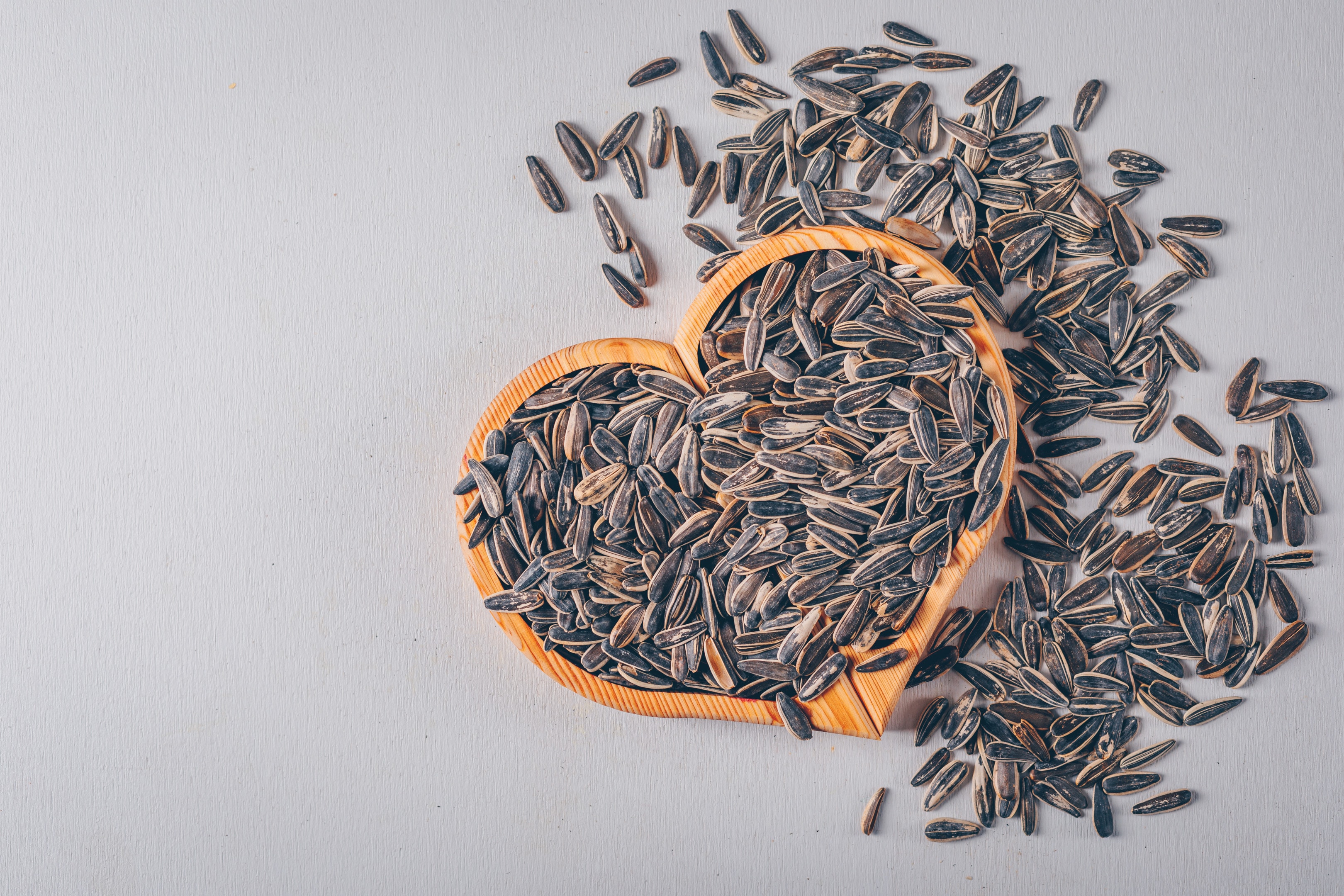 Black sunflower seeds on heart shaped board on gray background