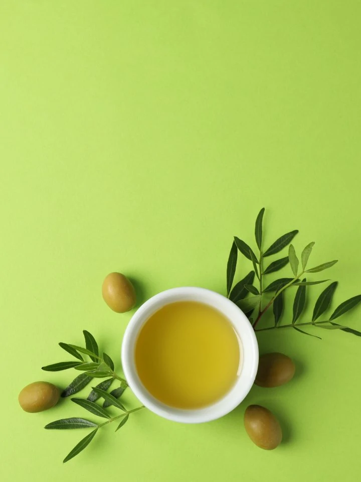 Bowl with olive oil and olives and olive leaves on green background