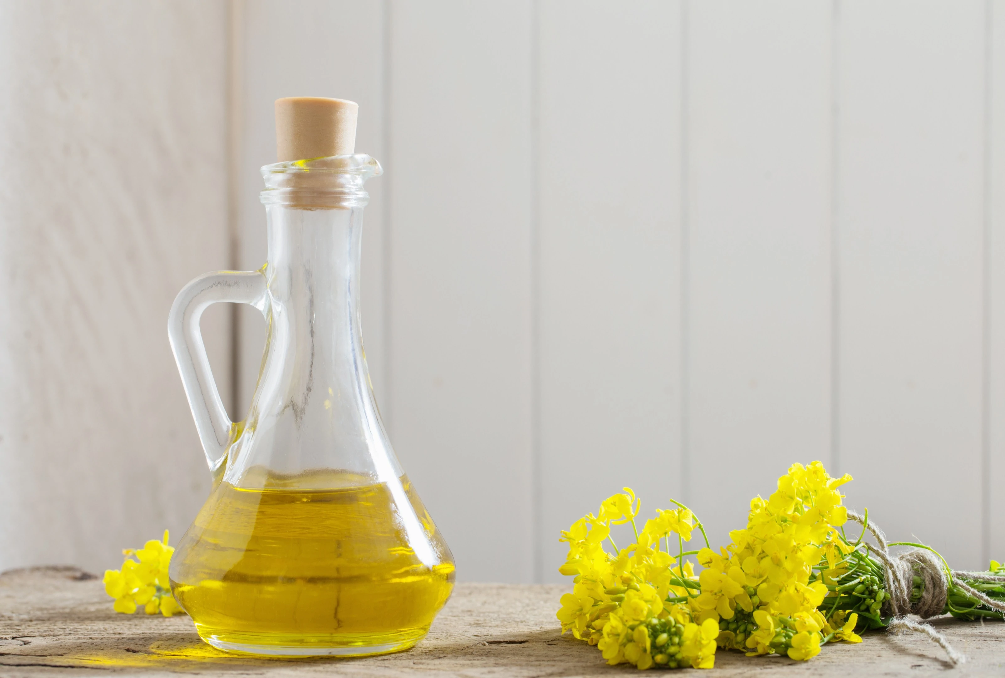 Canola oil with rape flowers on wooden table