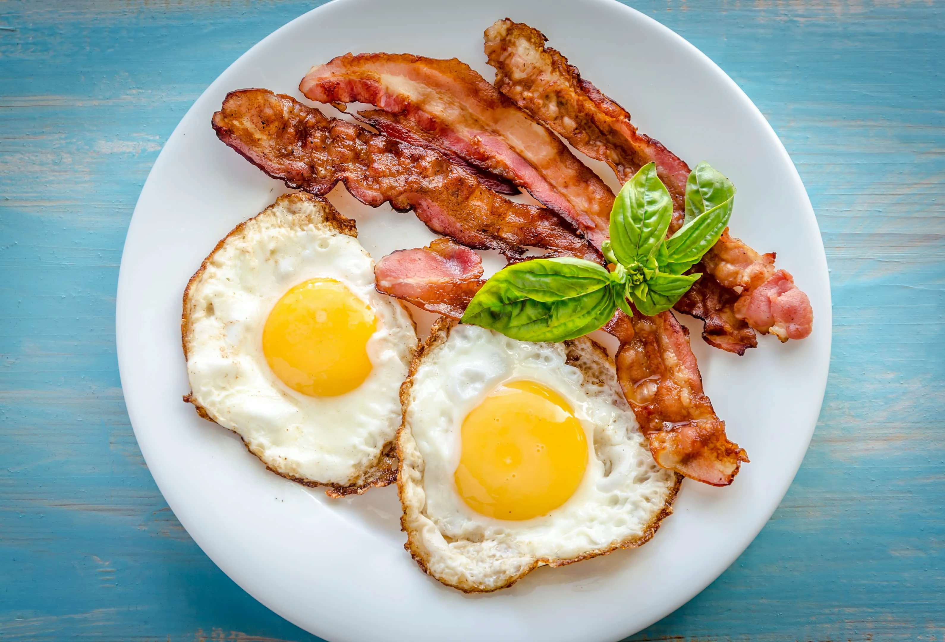 Fried eggs with fried bacon on wooden table