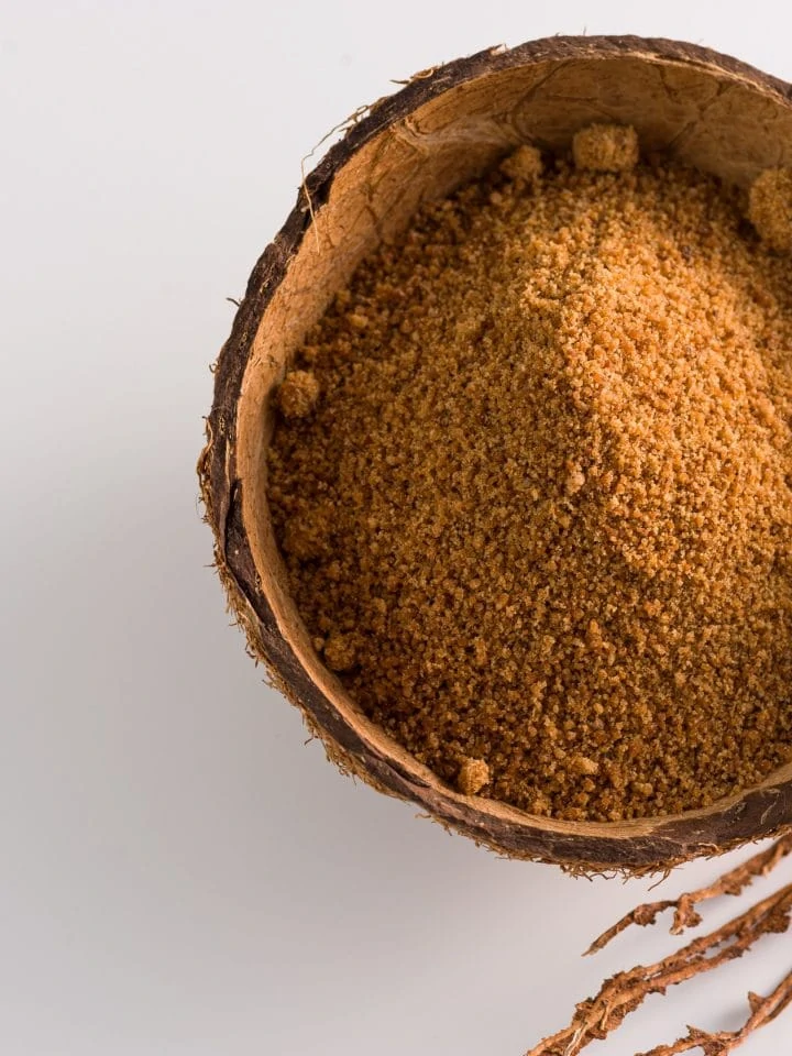 Natural granulated coconut sugar in coconut shell on white background