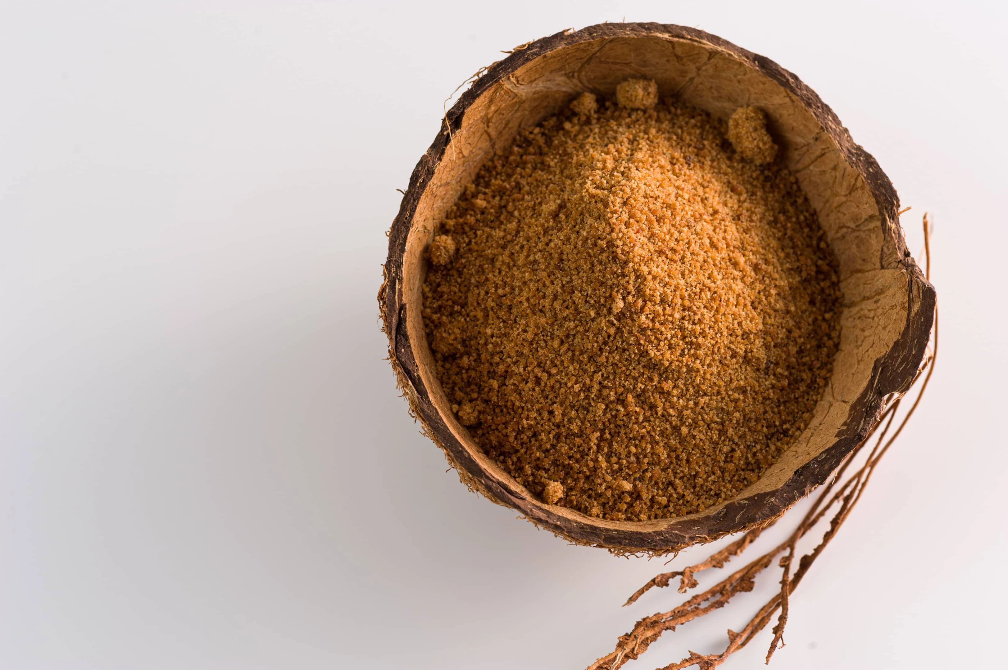 Natural granulated coconut sugar in coconut shell on white background