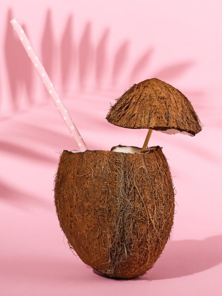 Open coconut with pink straw on pink background