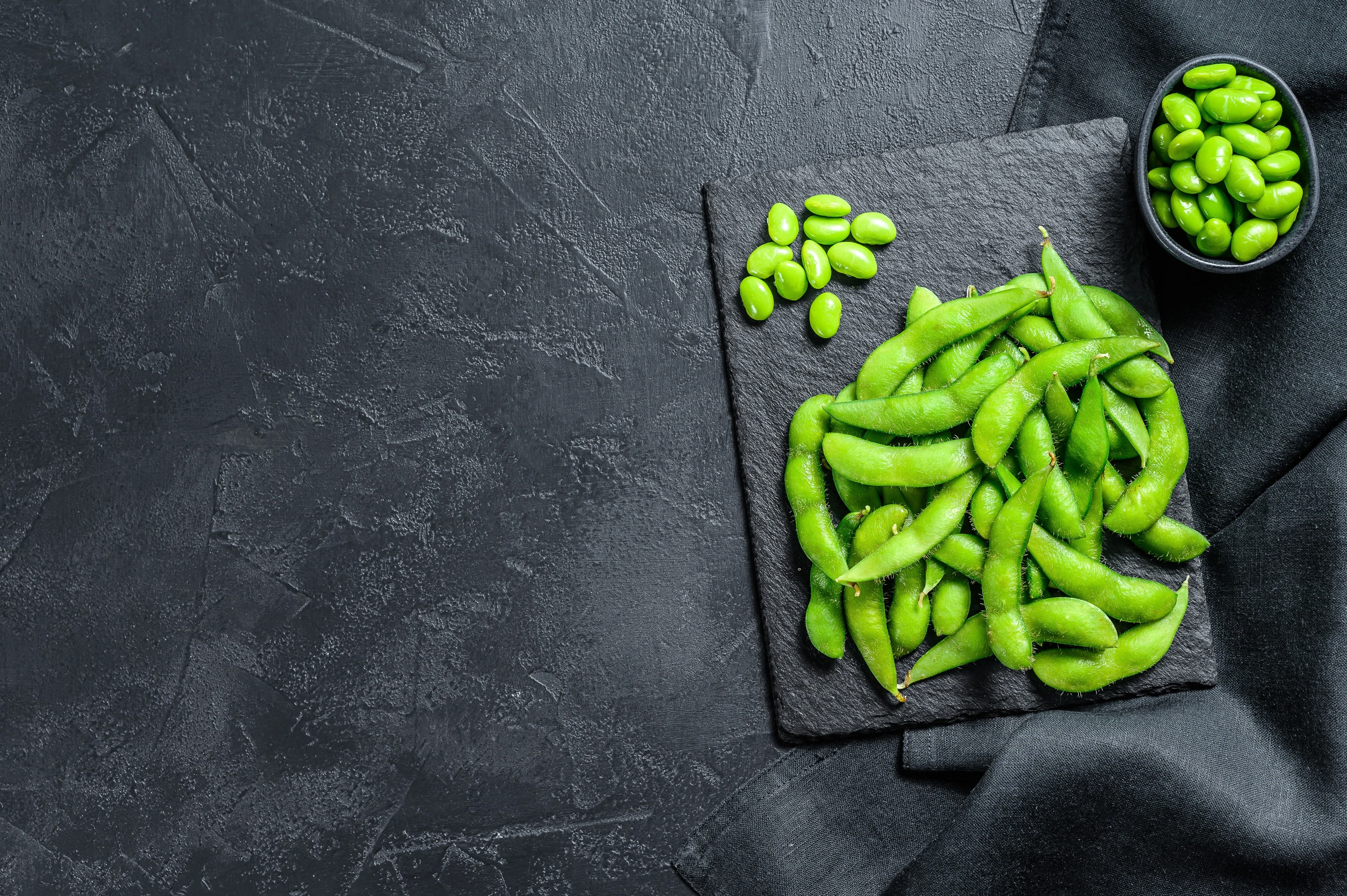 Raw green edamame soybeans on black stone plate