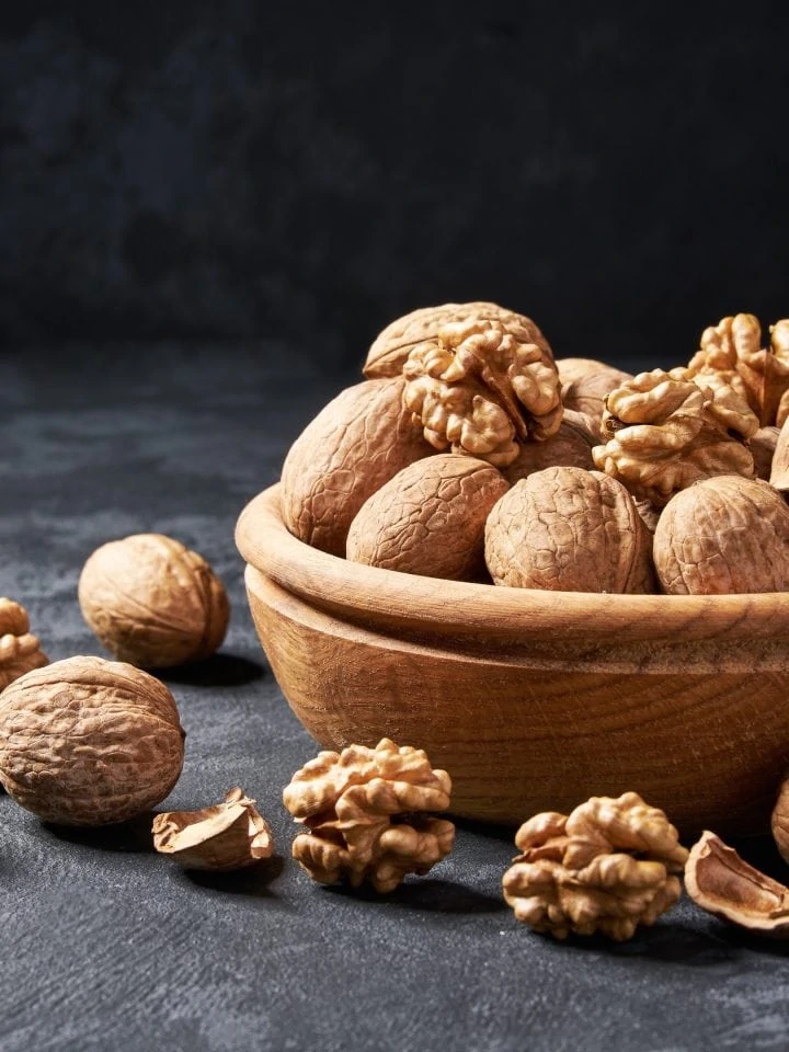 Raw walnuts in wooden bowl on dark table