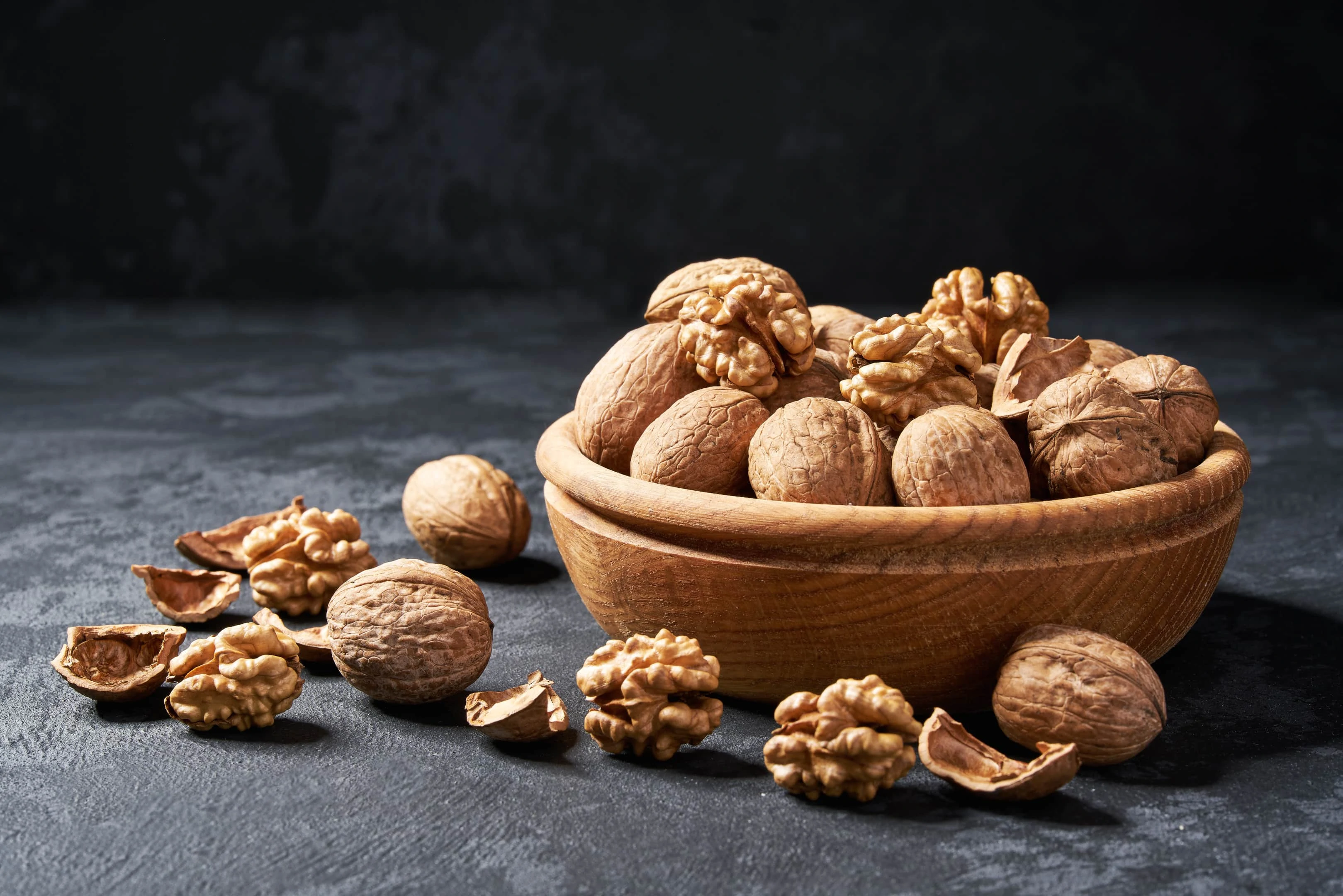 Raw walnuts in wooden bowl on dark table