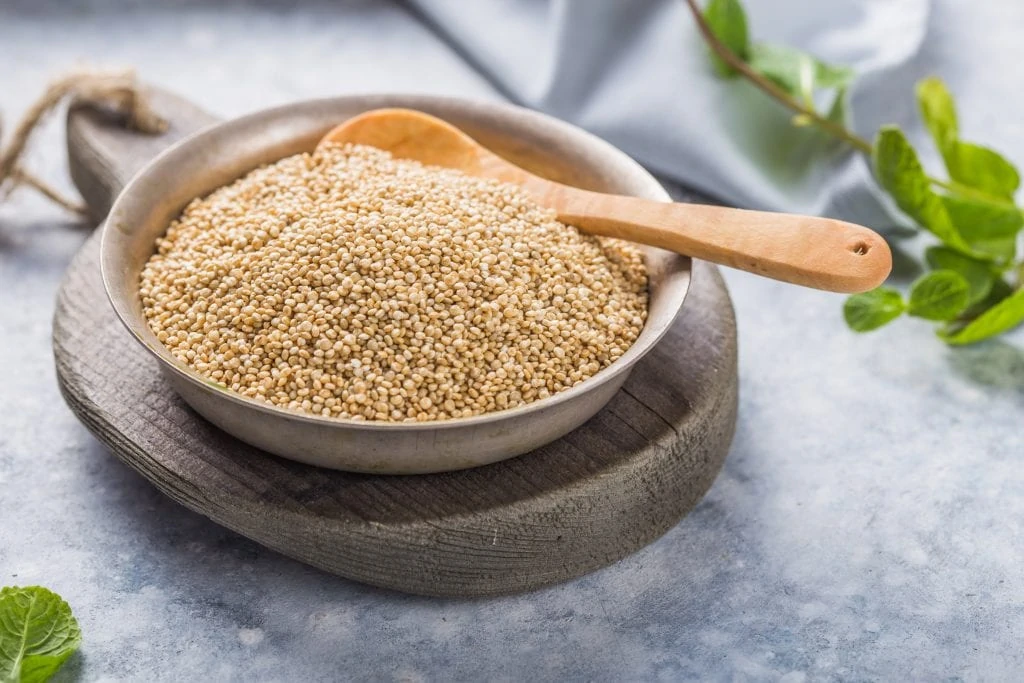 Raw white quinoa seeds in plate with wooden spoon