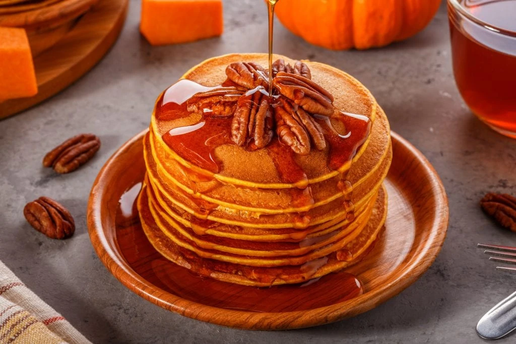 Stack pumpkin pancakes with pecans and maple syrup