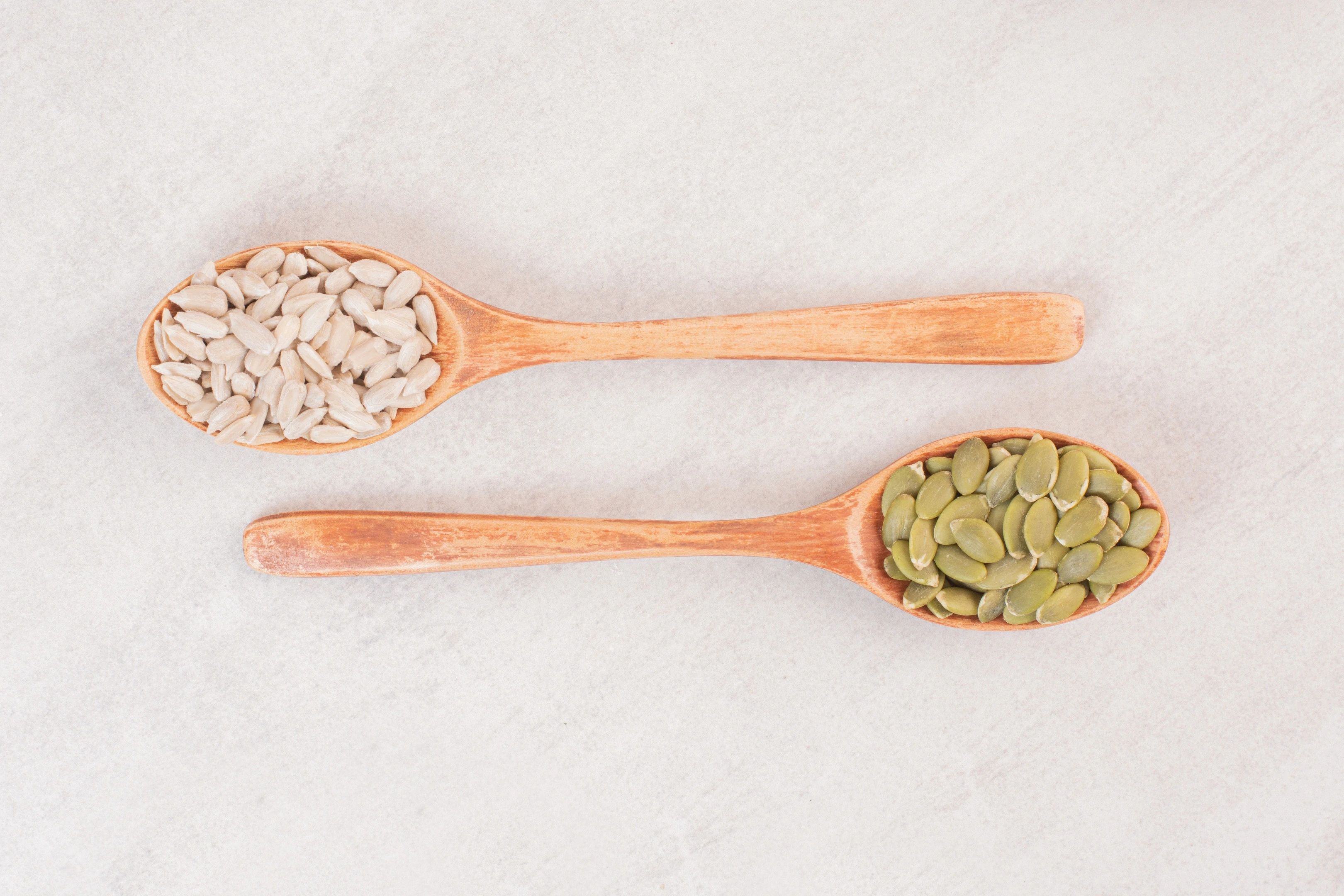 Two wooden spoon with sunflower and pumpkin seeds on white surface