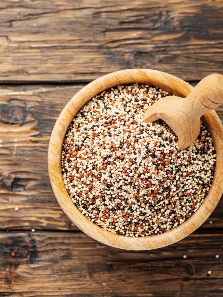 Uncooked quinoa in wooden bowl on wooden table