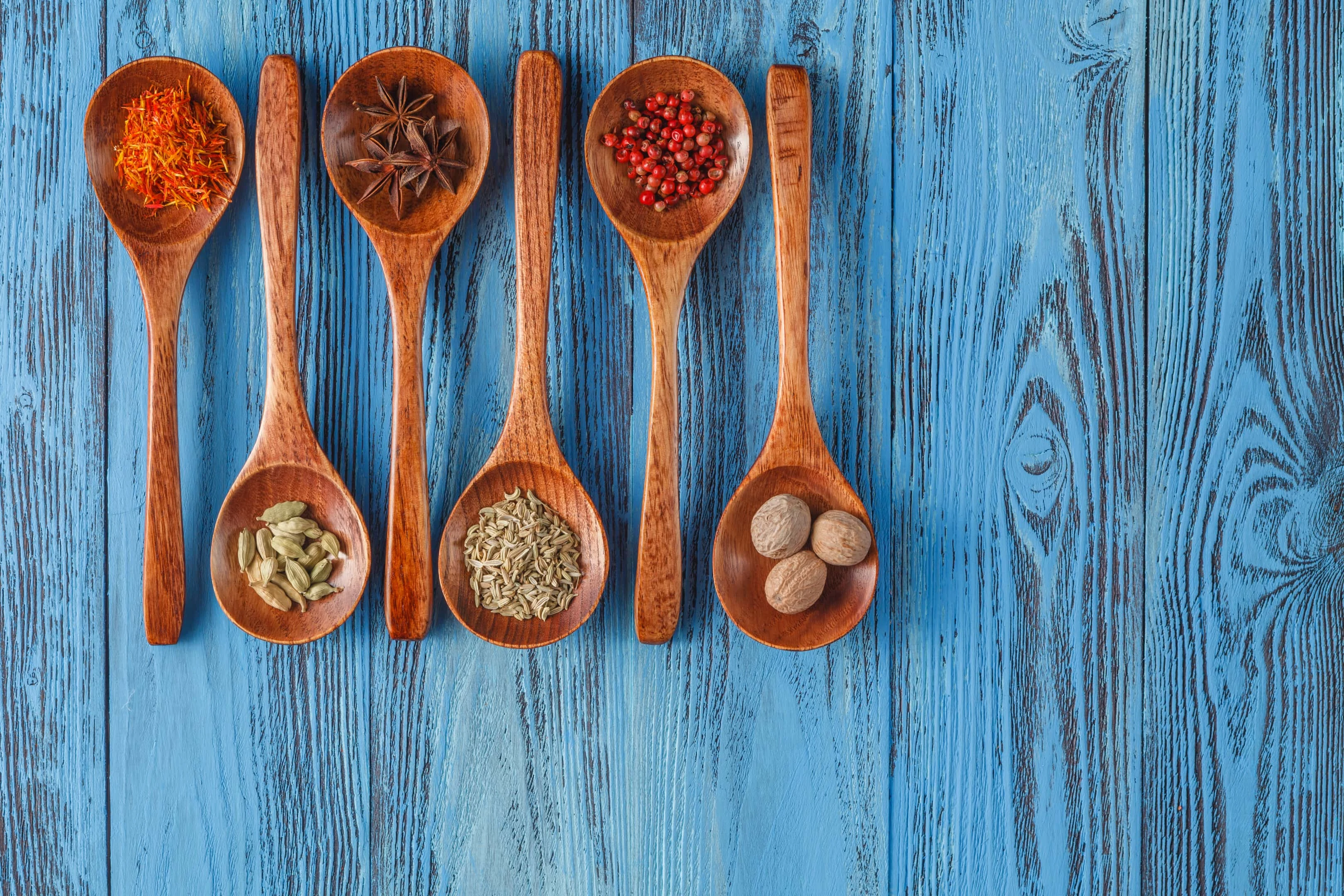 Various spice herbs in wooden spoons on wooden table