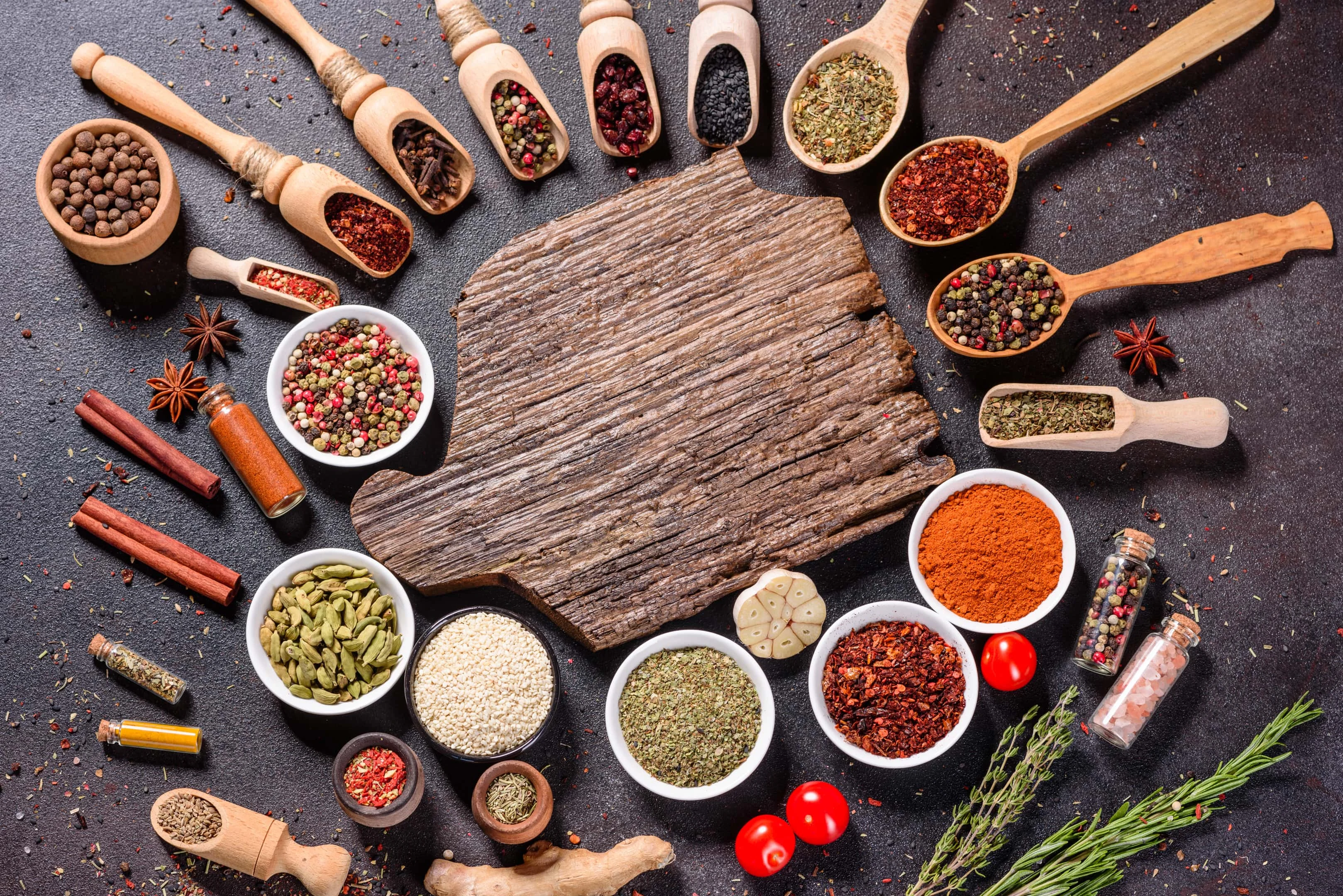 Various spices and herbs in wooden spoons surrounding wooden board