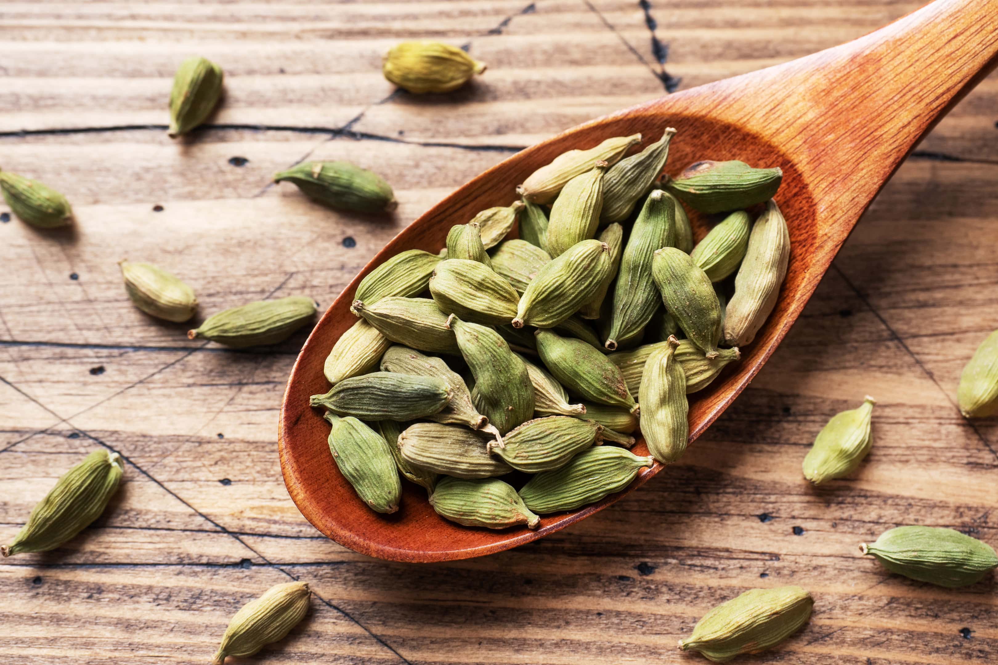Whole grains cardamom in wooden spoon on wooden table