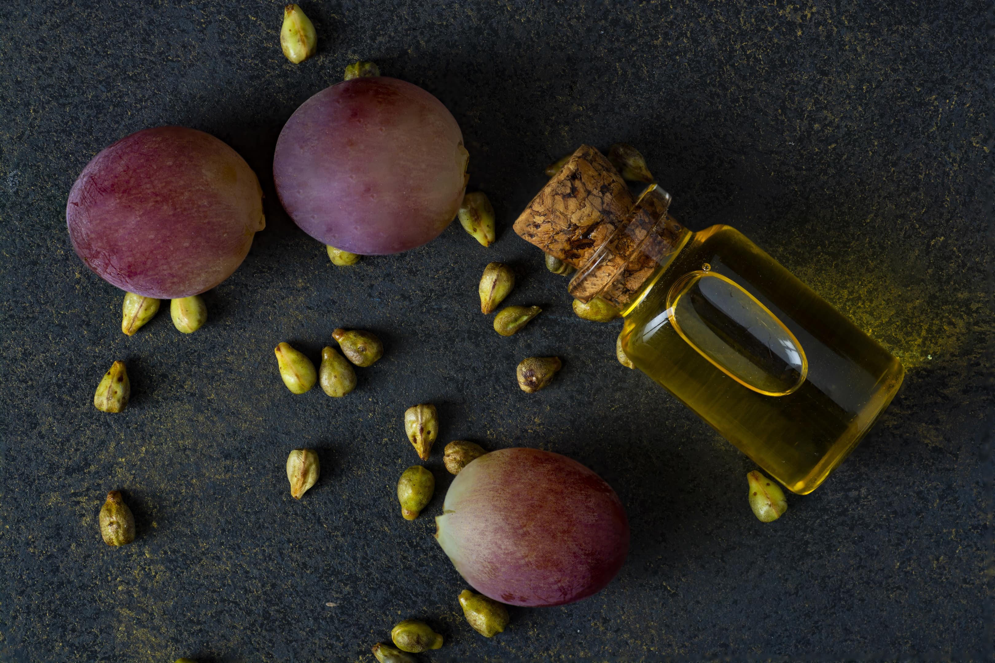 Bottle of grape oil with grape grains and pink grapes